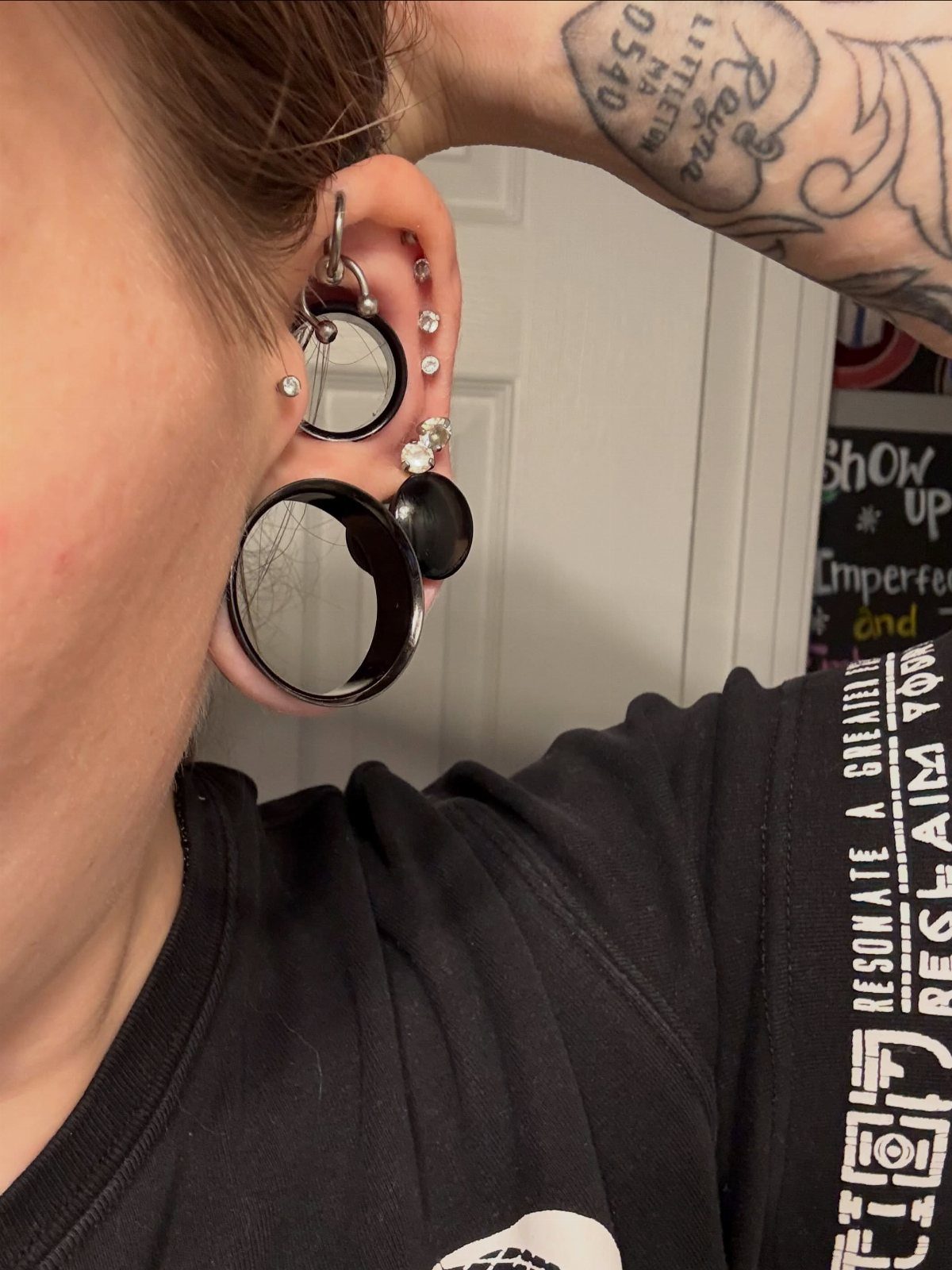 Ear with multiple piercings including large black gauges and small silver studs