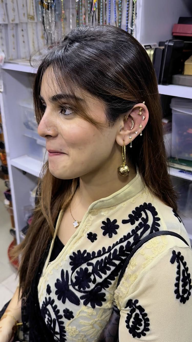 Woman with multiple gold helix and lobe piercings wearing an embroidered cream top.
