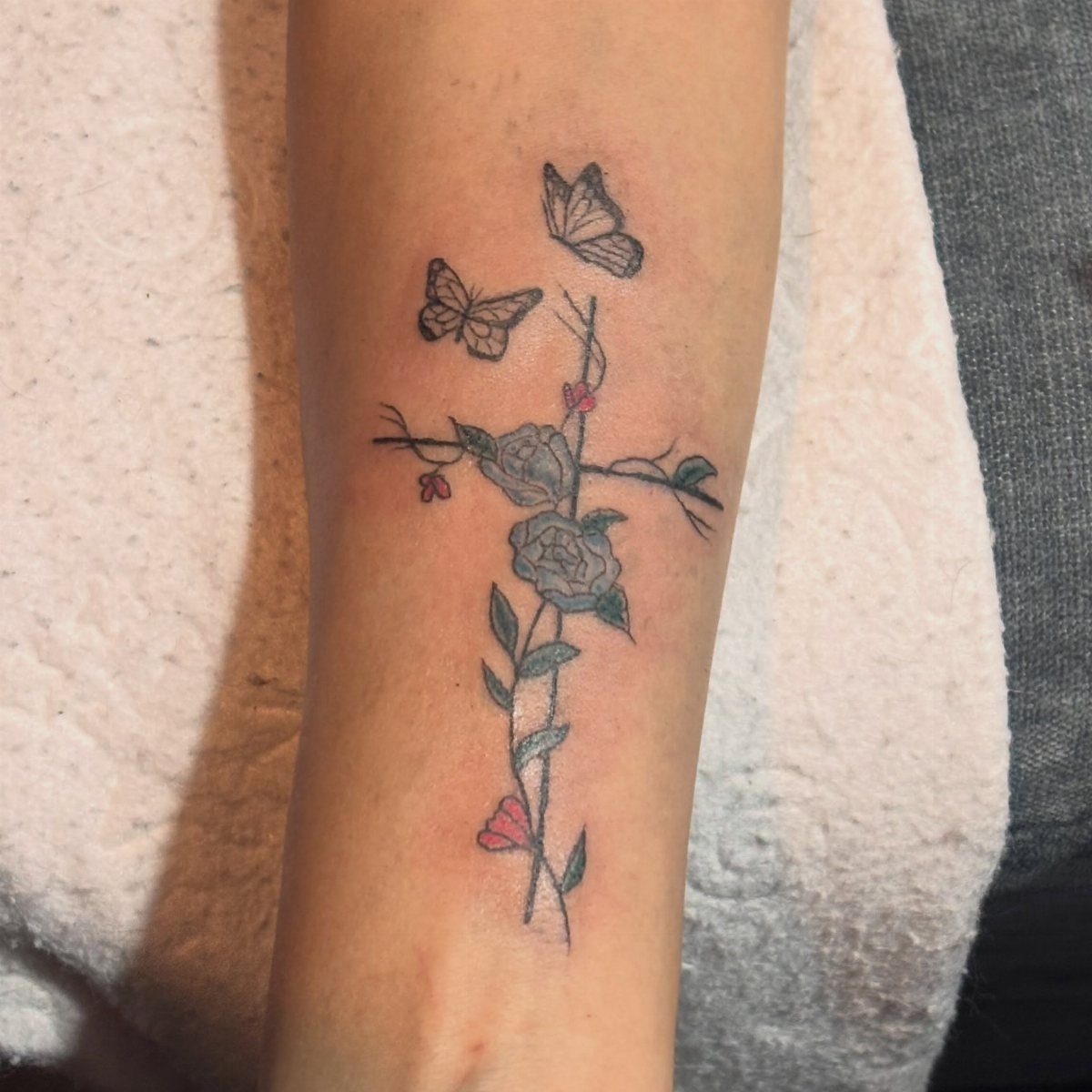Cross tattoo with grey roses and two butterflies on a person's leg