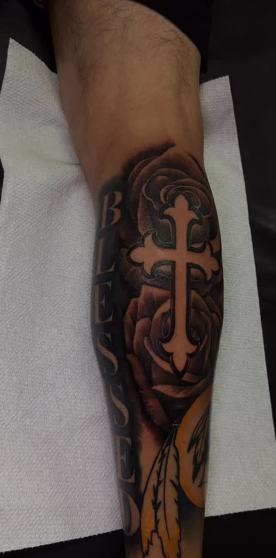 Cross tattoo on a leg with a rose and the word BLESSED in script