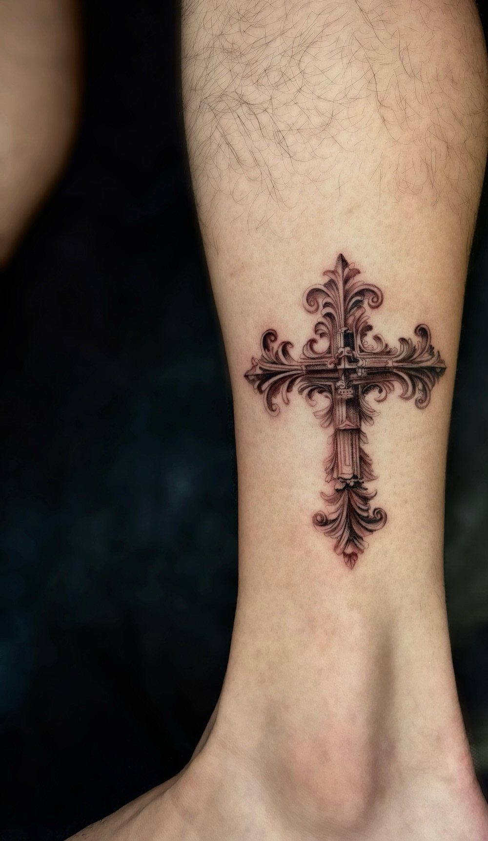 Ornate gothic cross tattoo with intricate detailing on a person's lower leg.