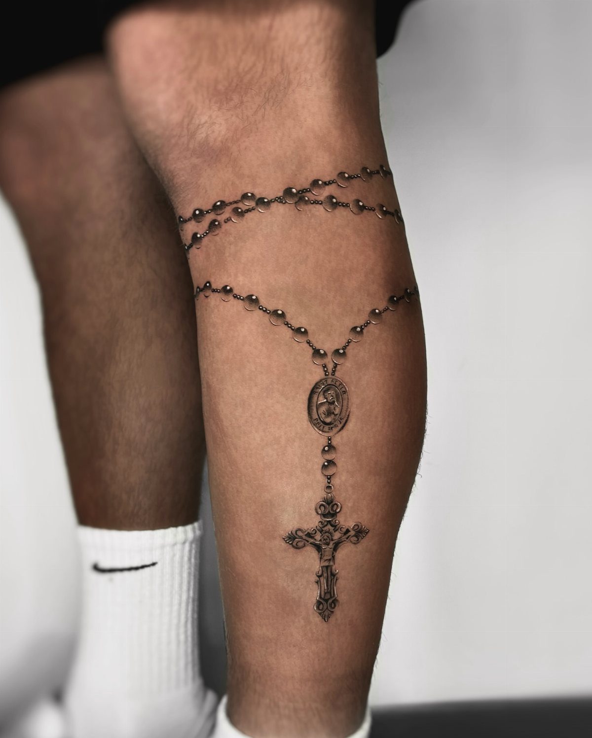 Rosary tattoo on a lower leg with beaded chains and a detailed cross.