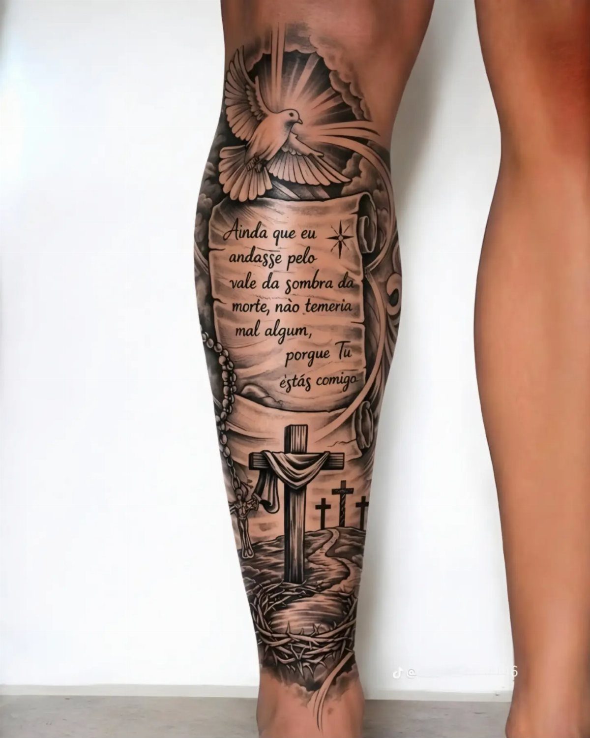 Three crosses tattoo on a leg with a dove and script text scroll.