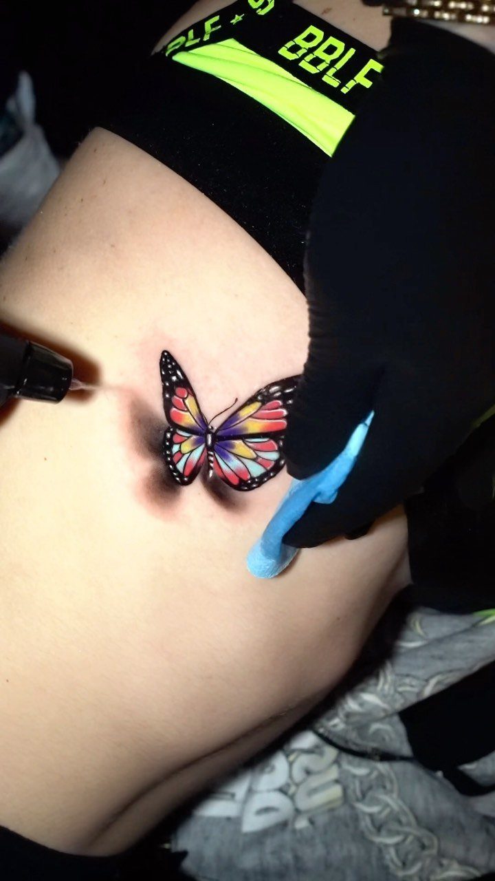 Colorful butterfly tattoo being applied to skin by an artist with black gloves