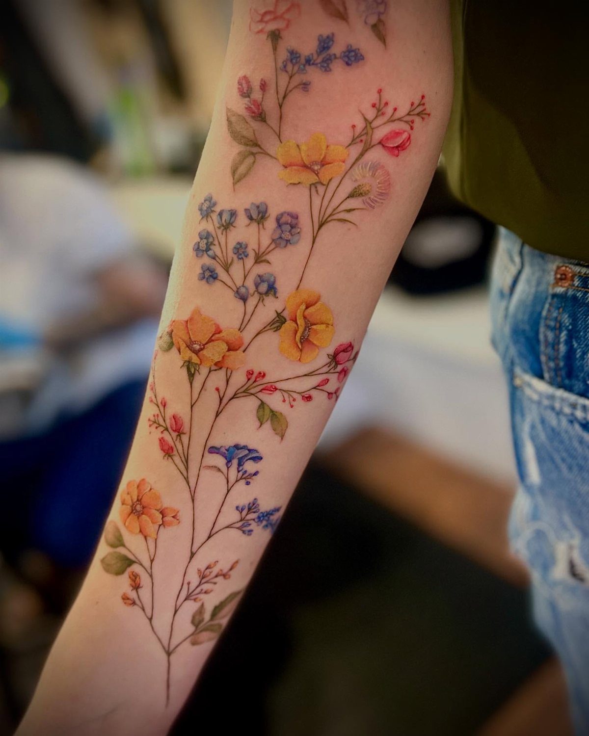 Colorful wildflower tattoo on a forearm with yellow, blue, and pink blossoms.