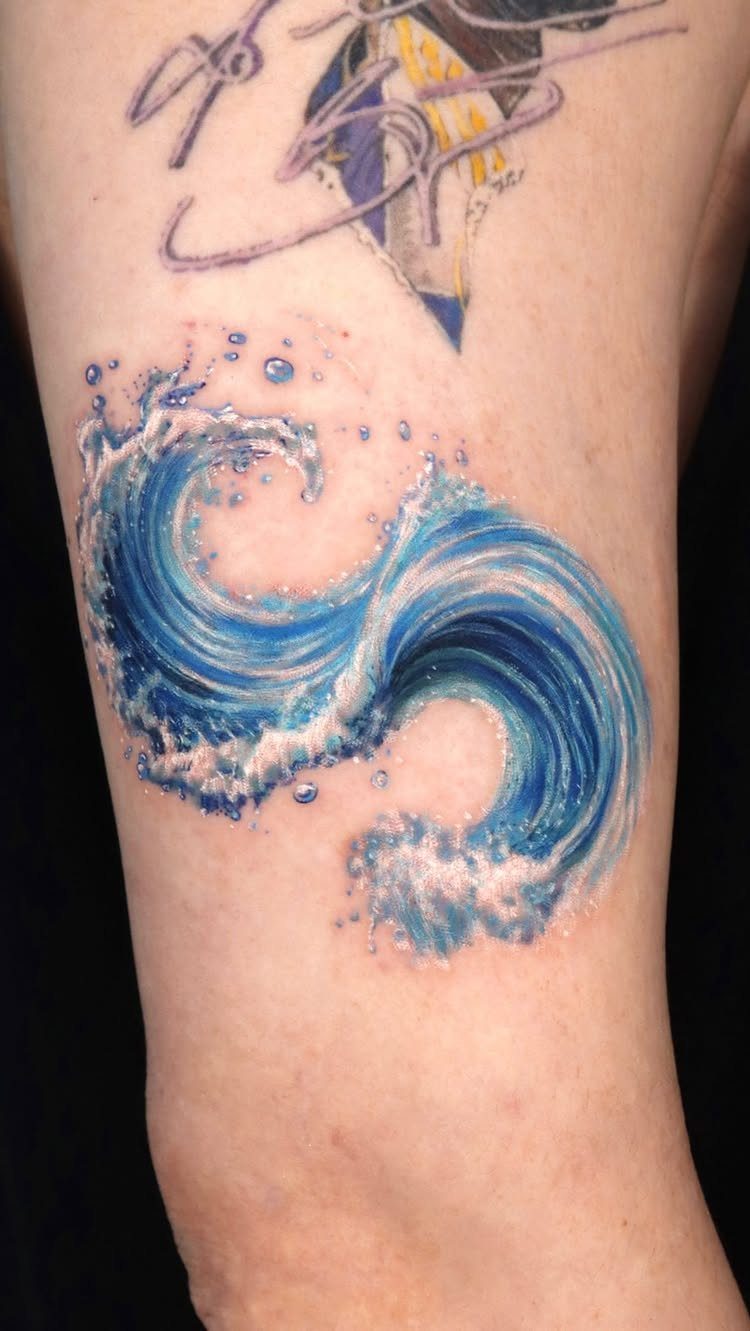 Blue ocean wave tattoo with white foam on a person's leg.