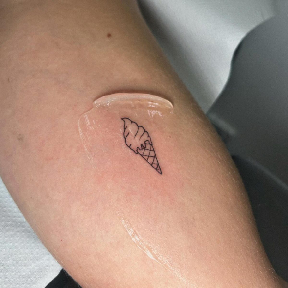 Small black ink ice cream cone tattoo on a person's arm with ointment.