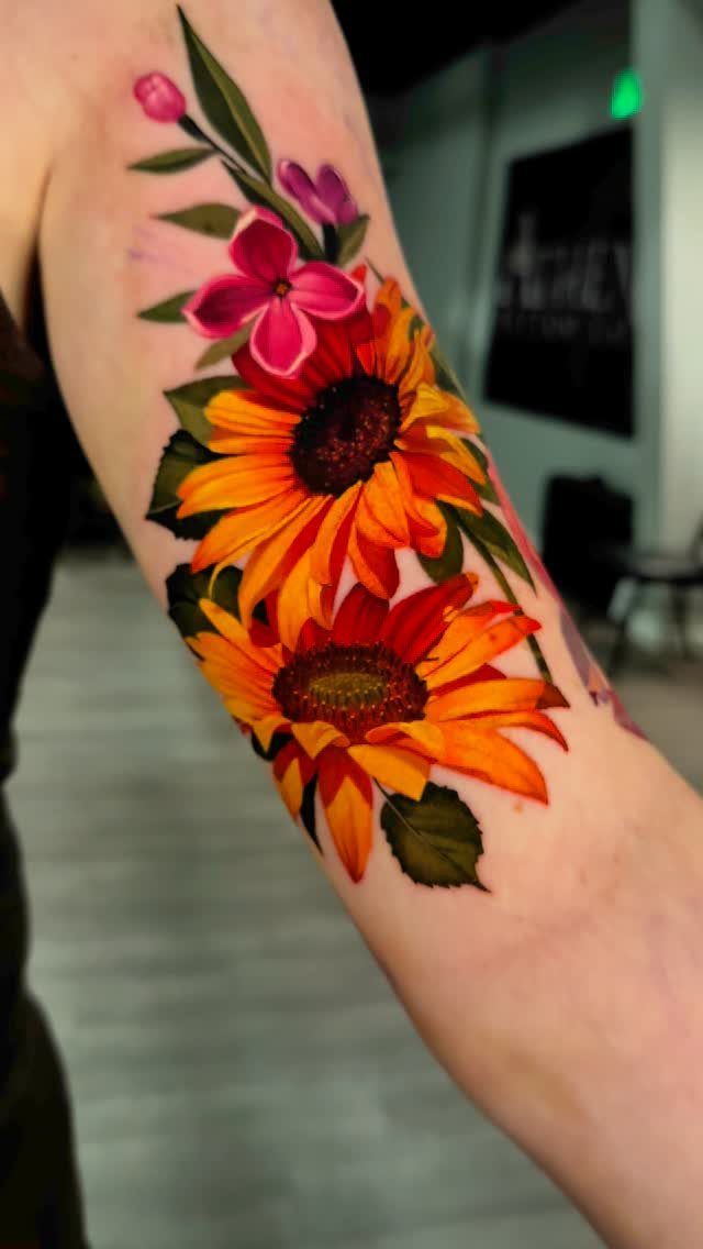 Sunflowers and pink flowers tattoo on a person's arm with vibrant orange and yellow colors