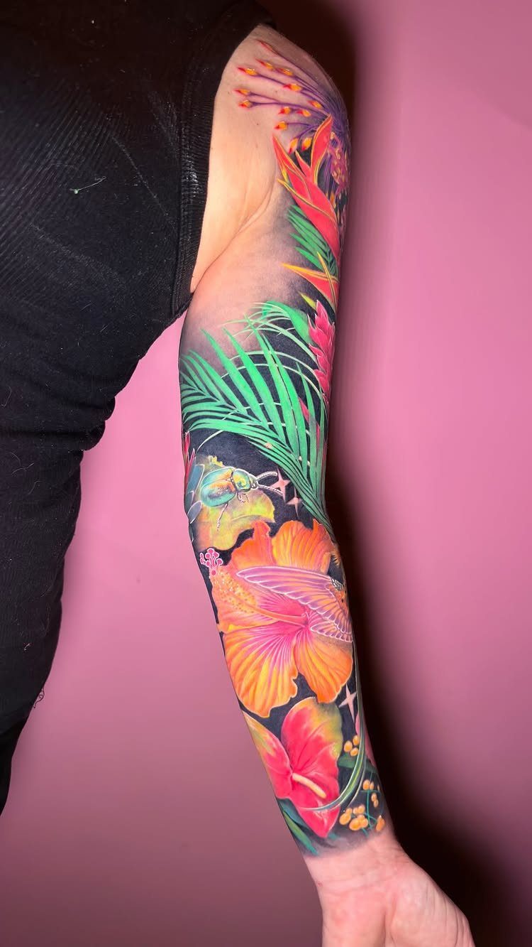 Colorful tropical tattoo sleeve with orange hibiscus flowers and green palm leaves on arm.