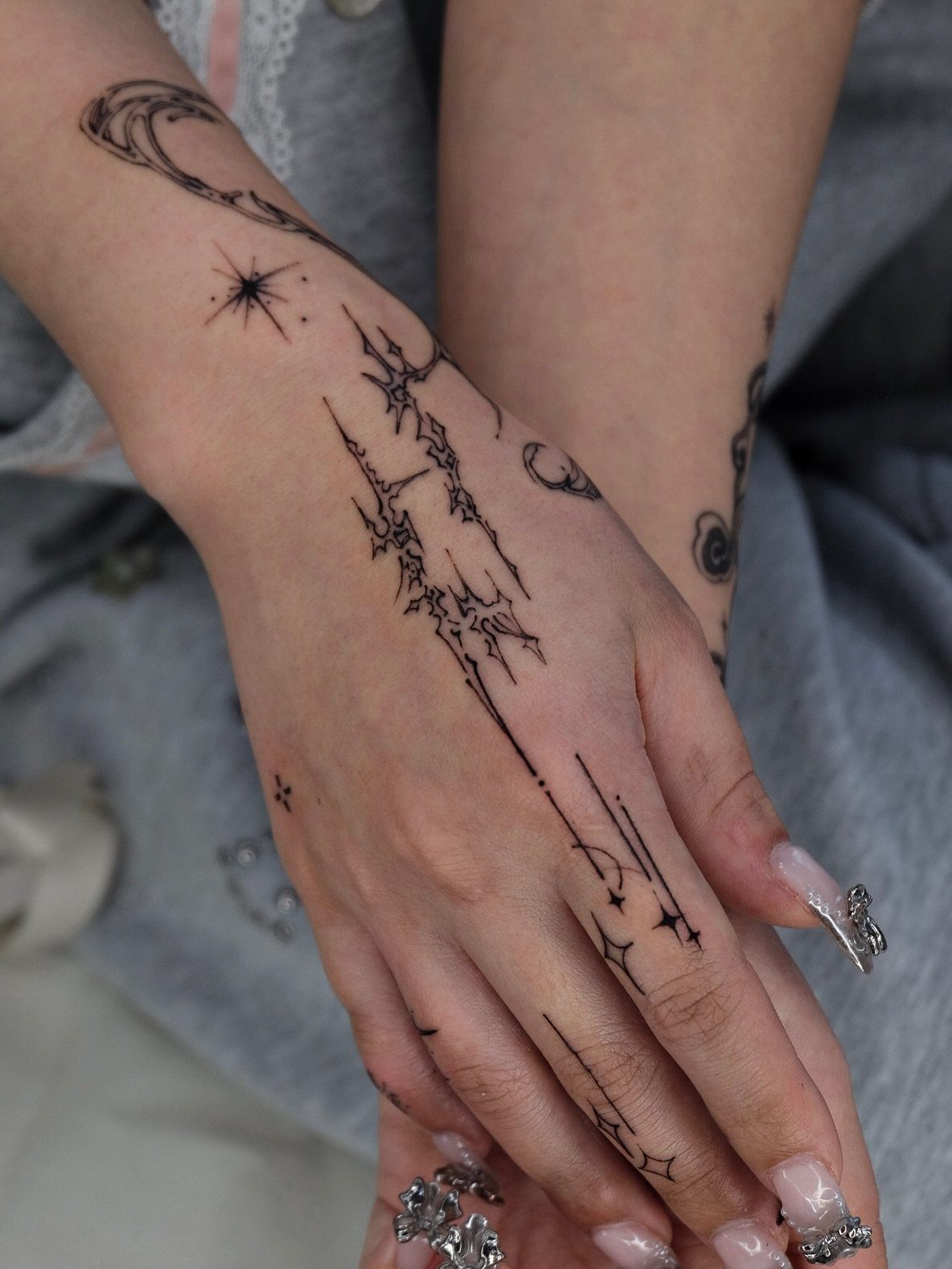 Hand and wrist with sharp black cybersigilism tattoos and silver rings