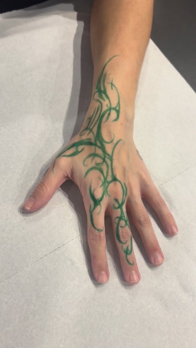 Hand and wrist with a green cybersigilism tattoo featuring sharp, flowing organic lines.