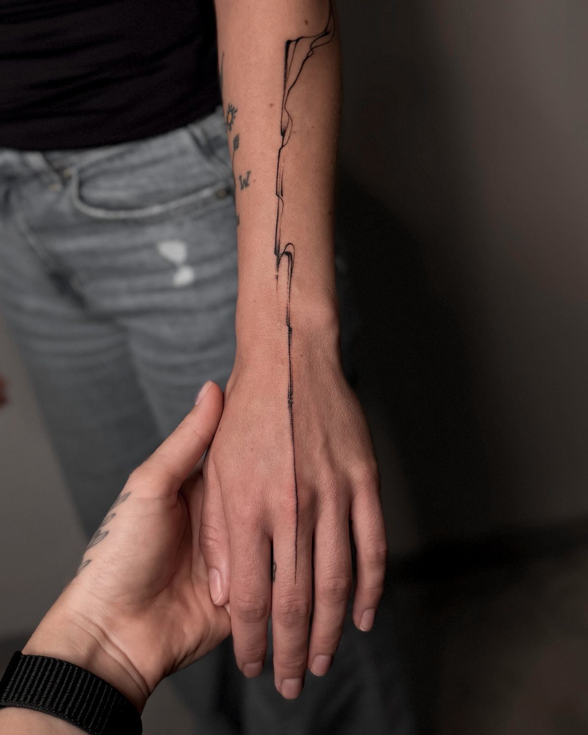 Hand and forearm with a sharp organic black line tattoo extending to the finger.
