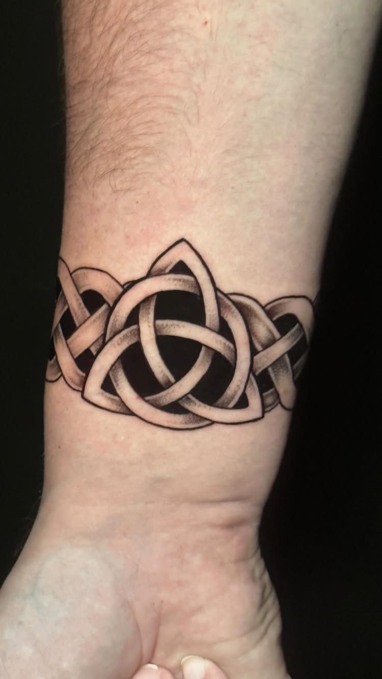 Celtic knot tattoo on a wrist featuring a central triquetra and interlocking patterns.
