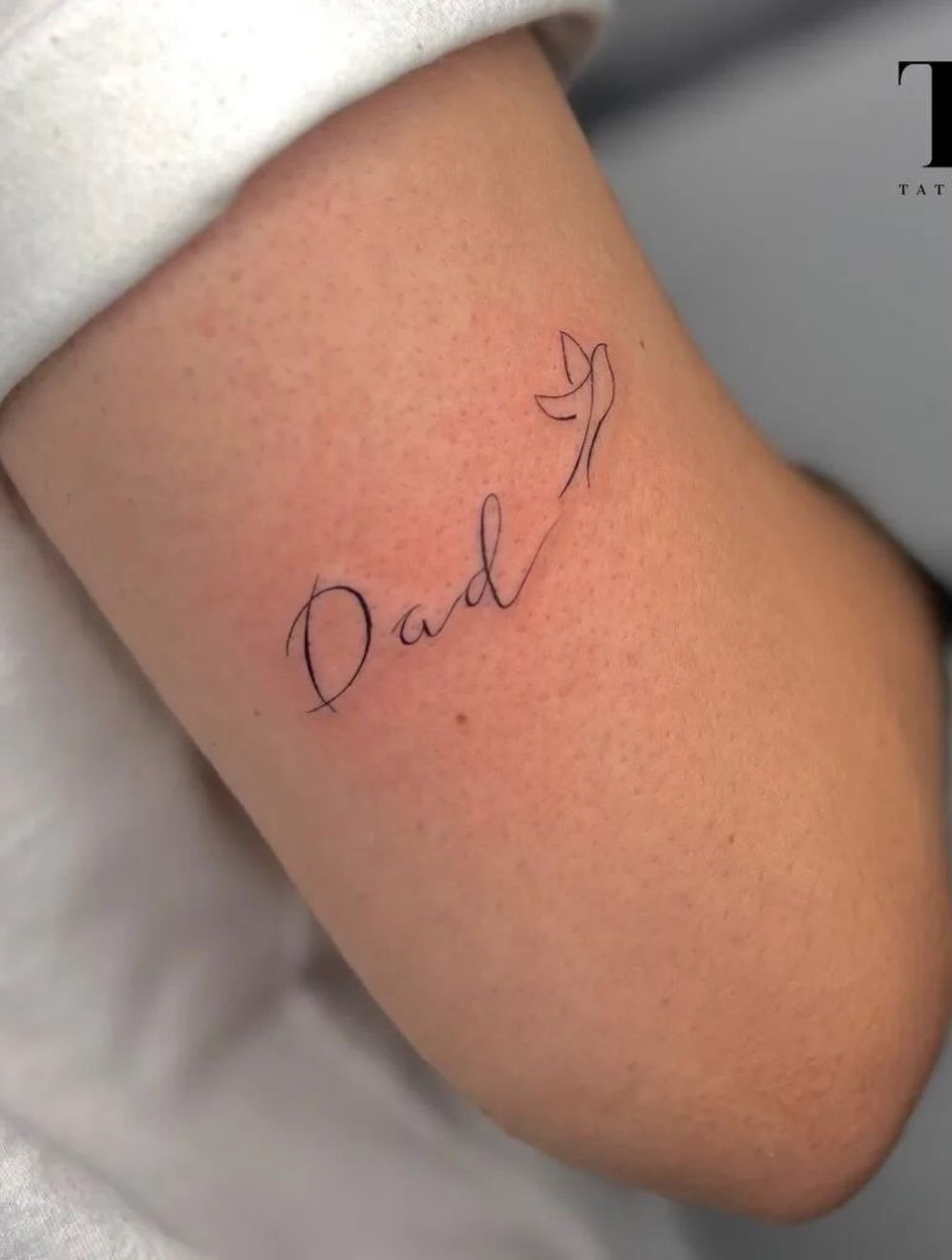 Cursive Dad tattoo with a small bird on a person's arm
