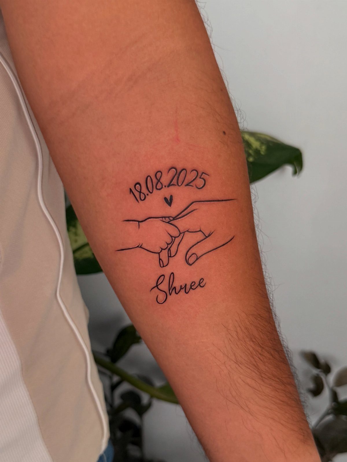 Tattoo on forearm showing a baby's hand holding a finger with name Shree