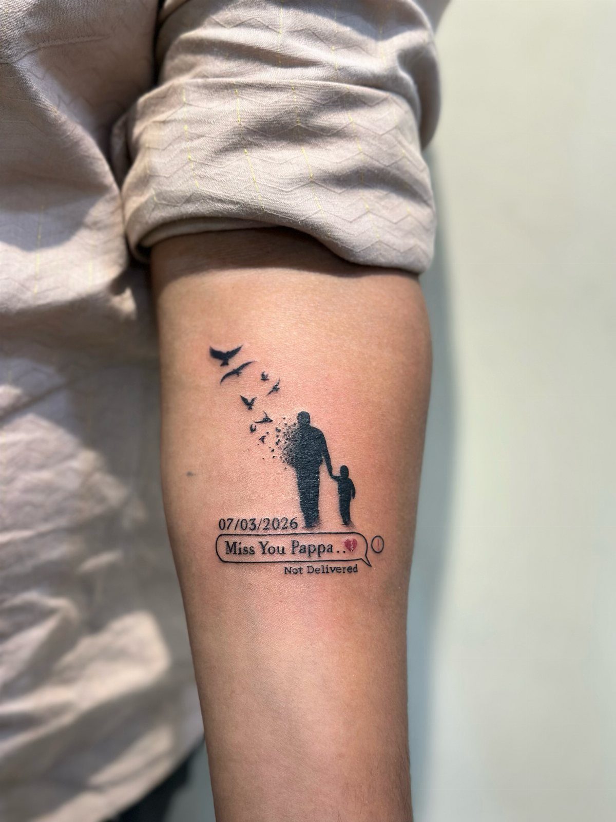 Tattoo on an arm showing a father and daughter silhouette with birds and text.