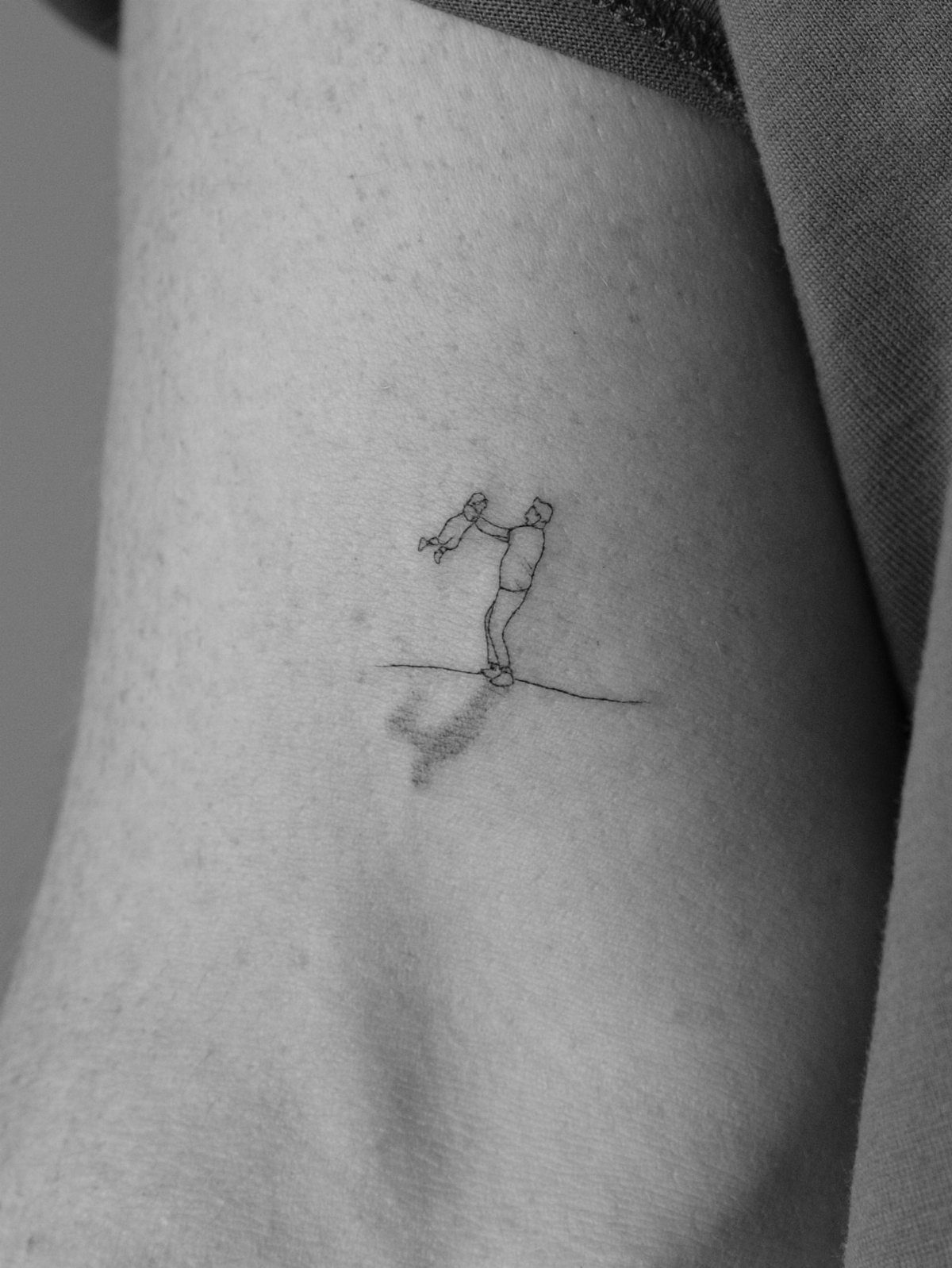 Minimalist line-art tattoo of a father lifting a child on a person's arm