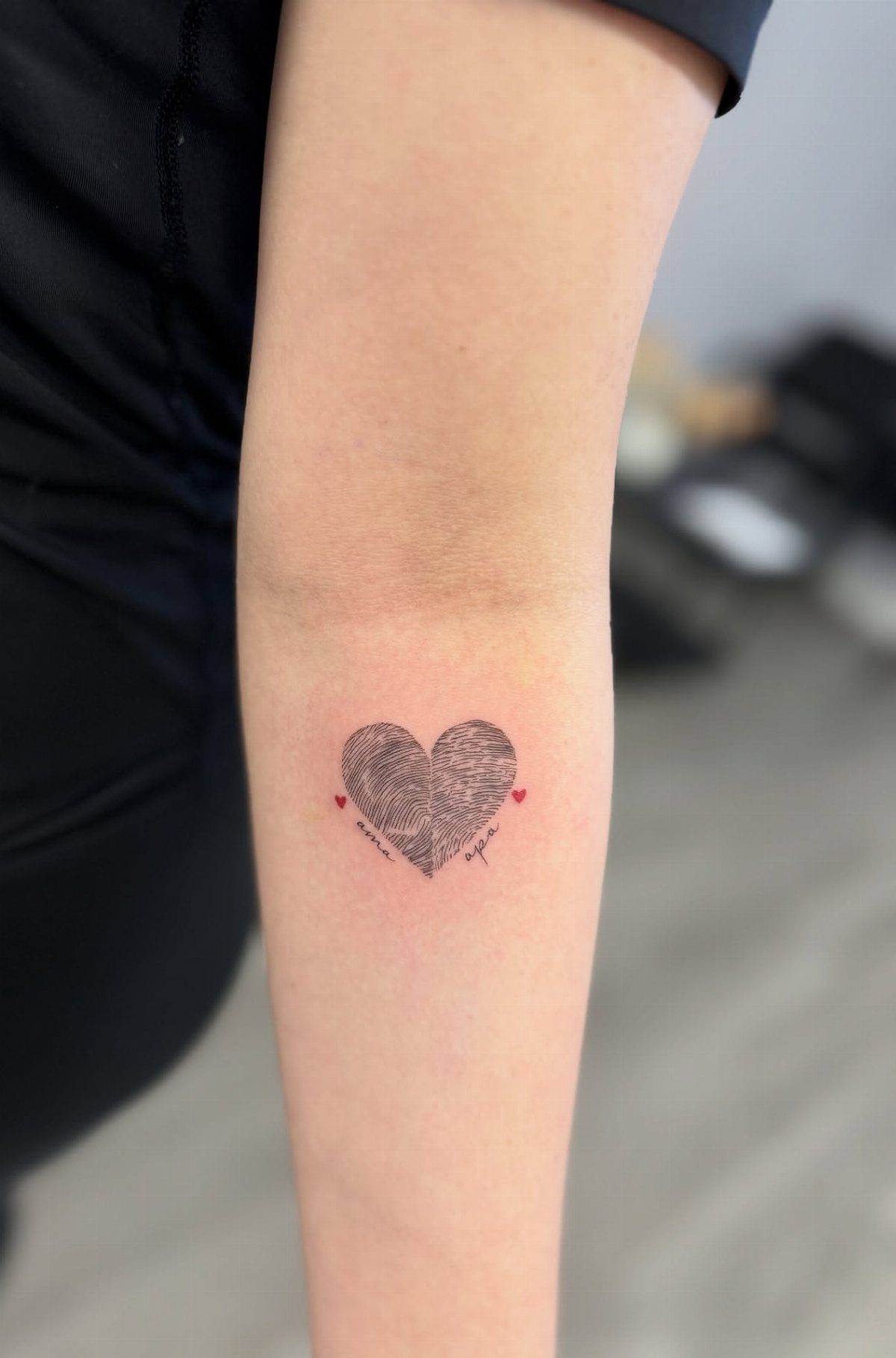 Heart tattoo made of fingerprints with small red hearts on a forearm.