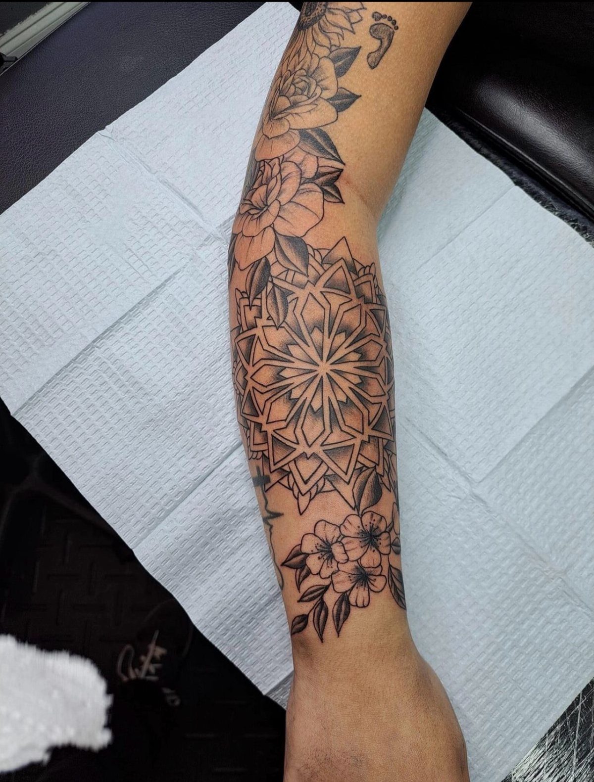 Forearm tattoo featuring a geometric mandala surrounded by detailed floral roses and blossoms.