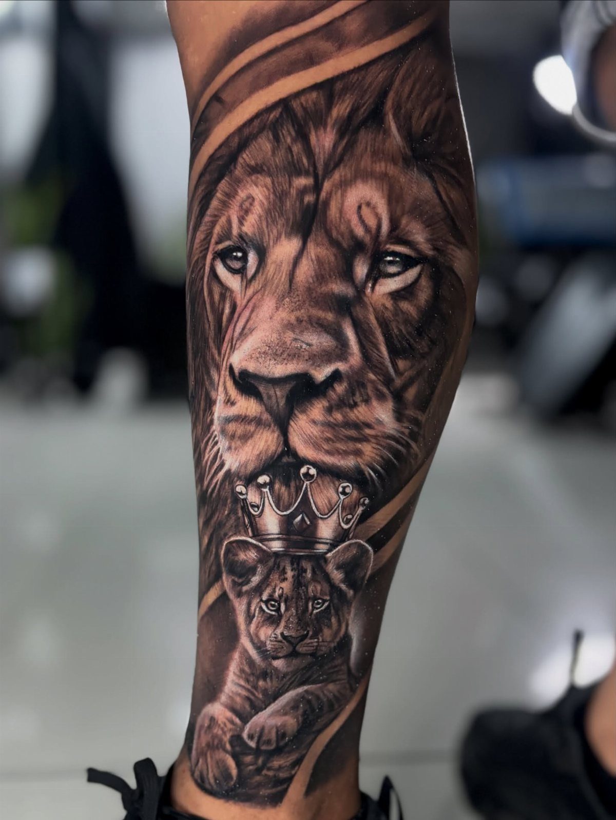 Lion and crowned cub tattoo in black and grey realism on a leg
