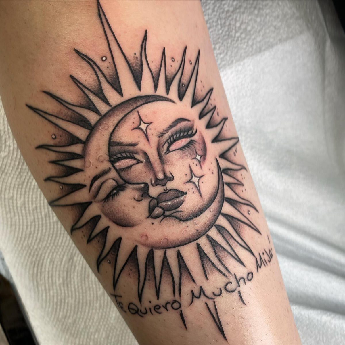 Sun and moon face tattoo with Spanish text on a person's arm