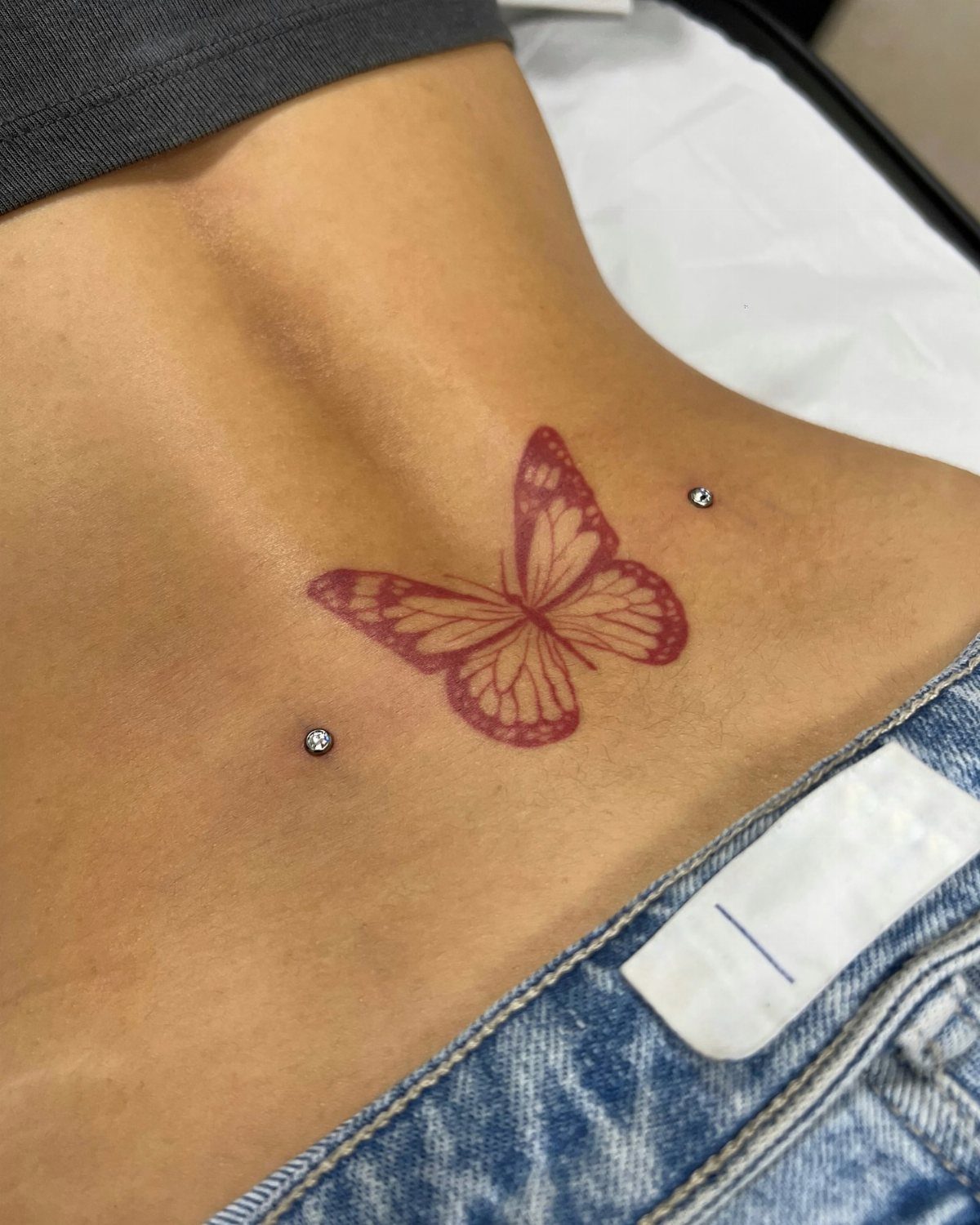 Dermal Piercing for Back Dimples: 7 Ideas and Jewelry 3 Lower back with red butterfly tattoo and two sparkling dermal piercings in dimples
