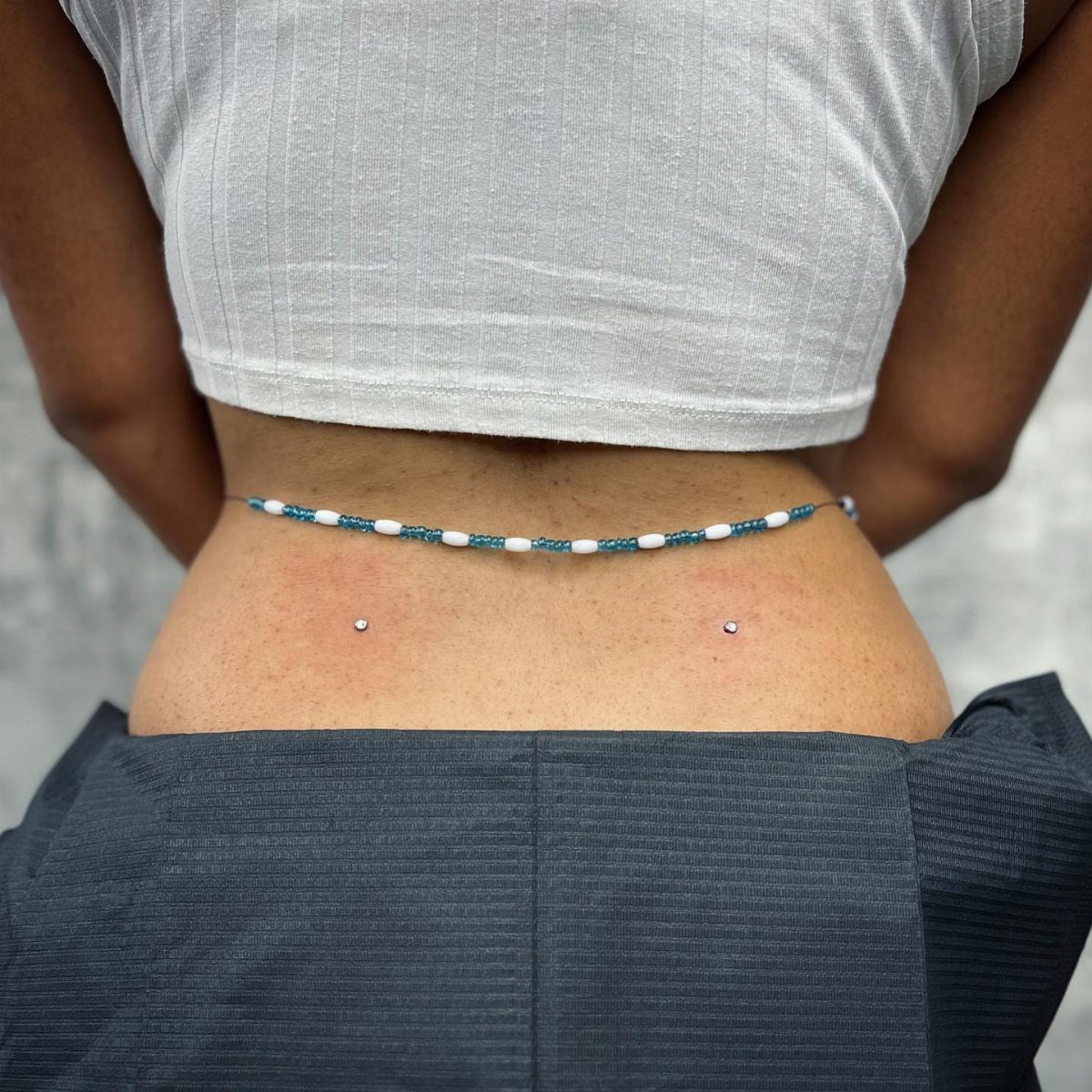 Dermal Piercing for Back Dimples: 7 Ideas and Jewelry 1 Two silver dermal piercings in the lower back dimples of a person.