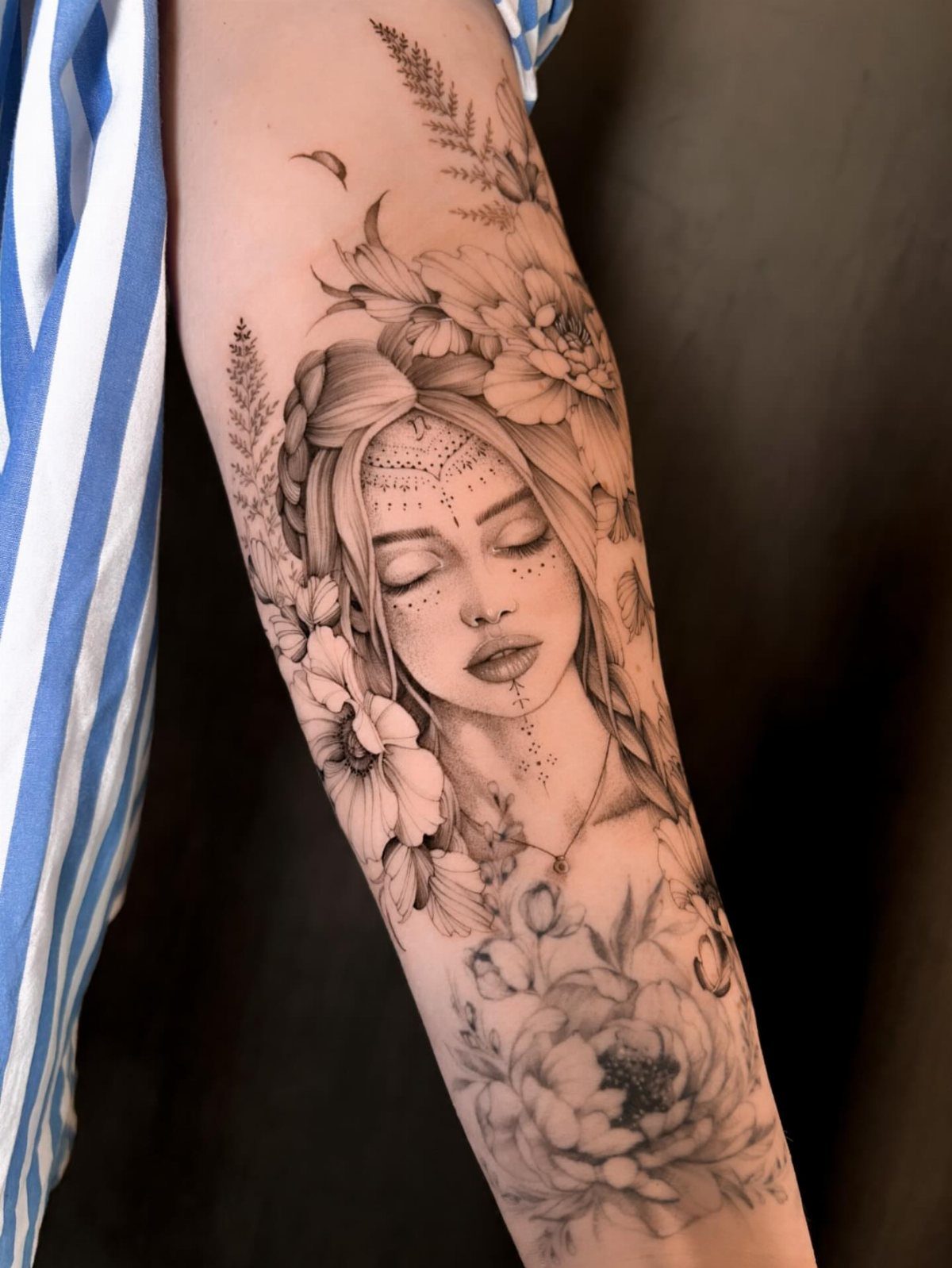 Detailed black and grey tattoo of a woman's face surrounded by blooming flowers.