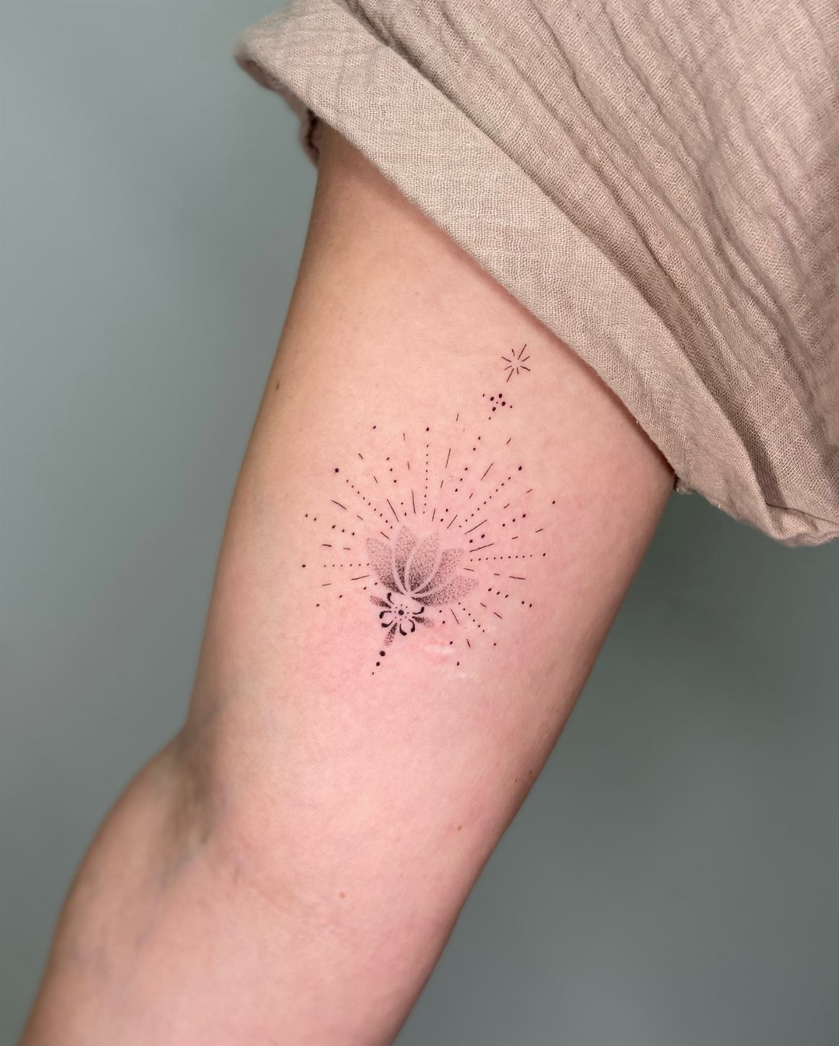 Delicate black ink flower tattoo with radiating dots on a person's arm.