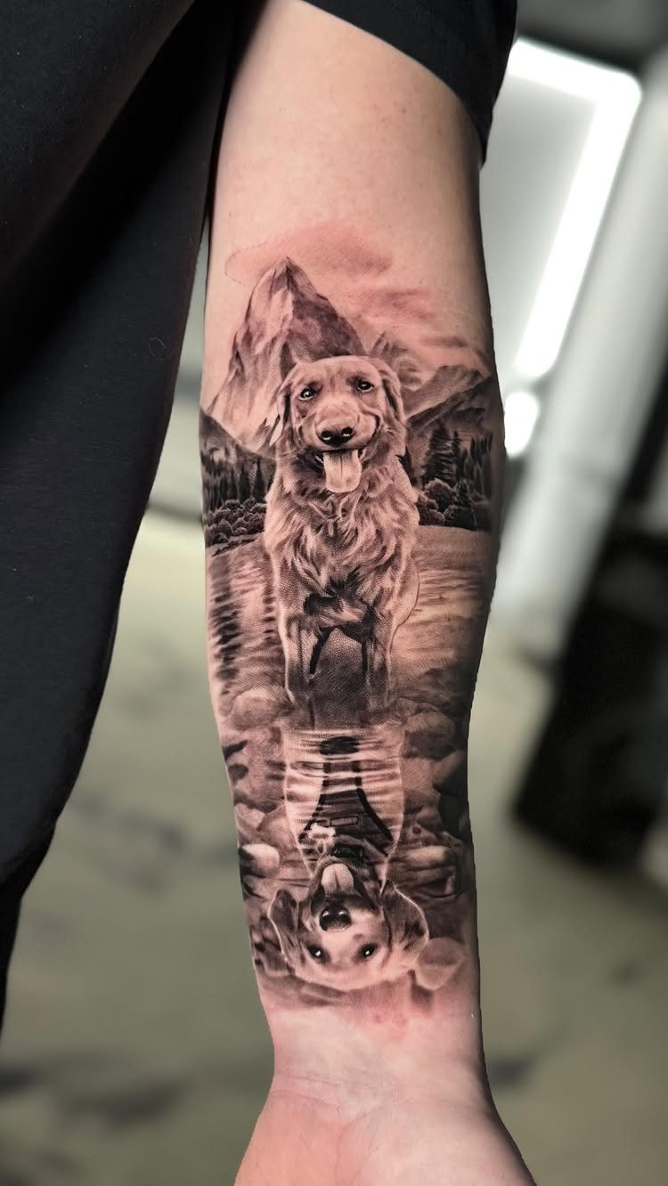 Realistic golden retriever portrait tattoo on a forearm with mountains and water reflection.
