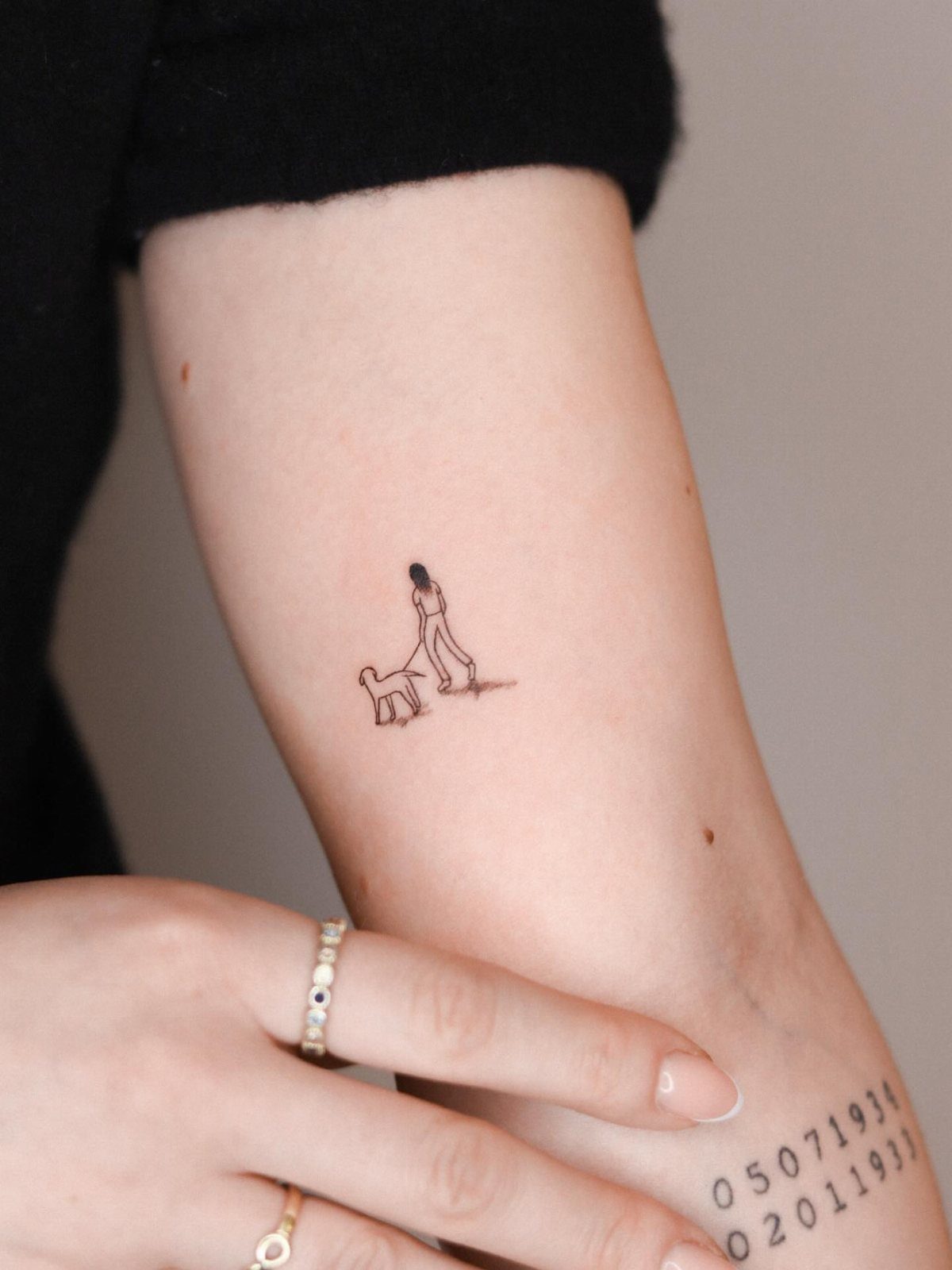 Tattoos on an arm showing a person walking a dog and two dates.