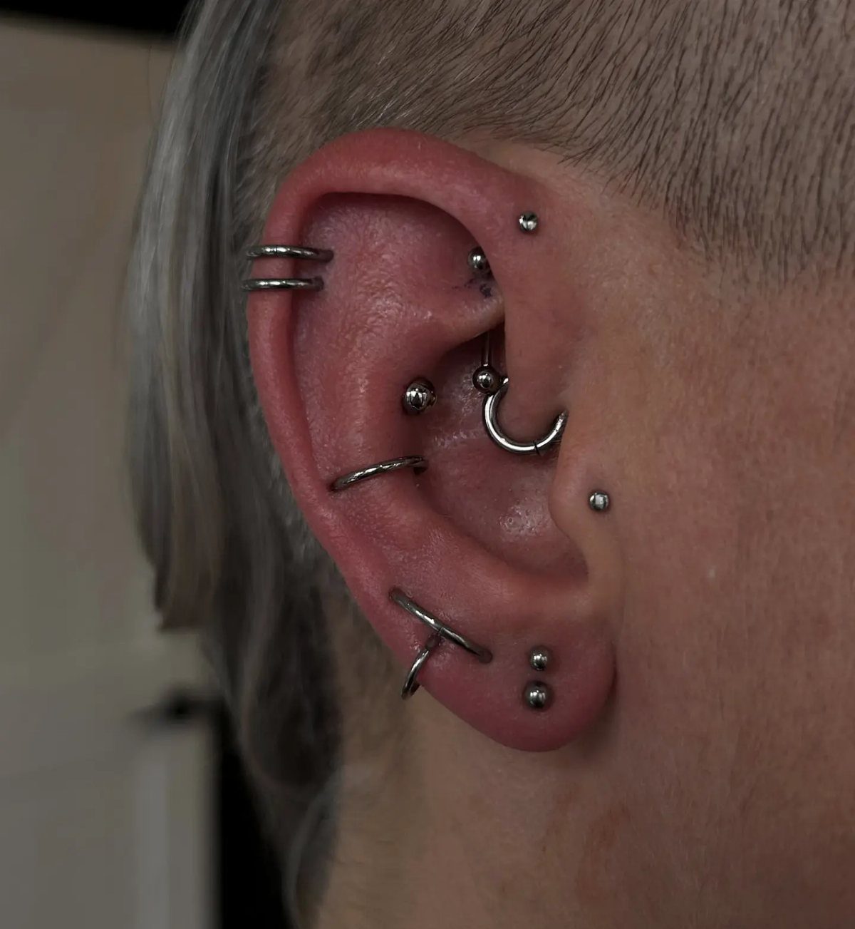 12 Ear Piercing Combo Ideas for Every Style 3 Human ear with a variety of silver rings and studs in multiple piercings.
