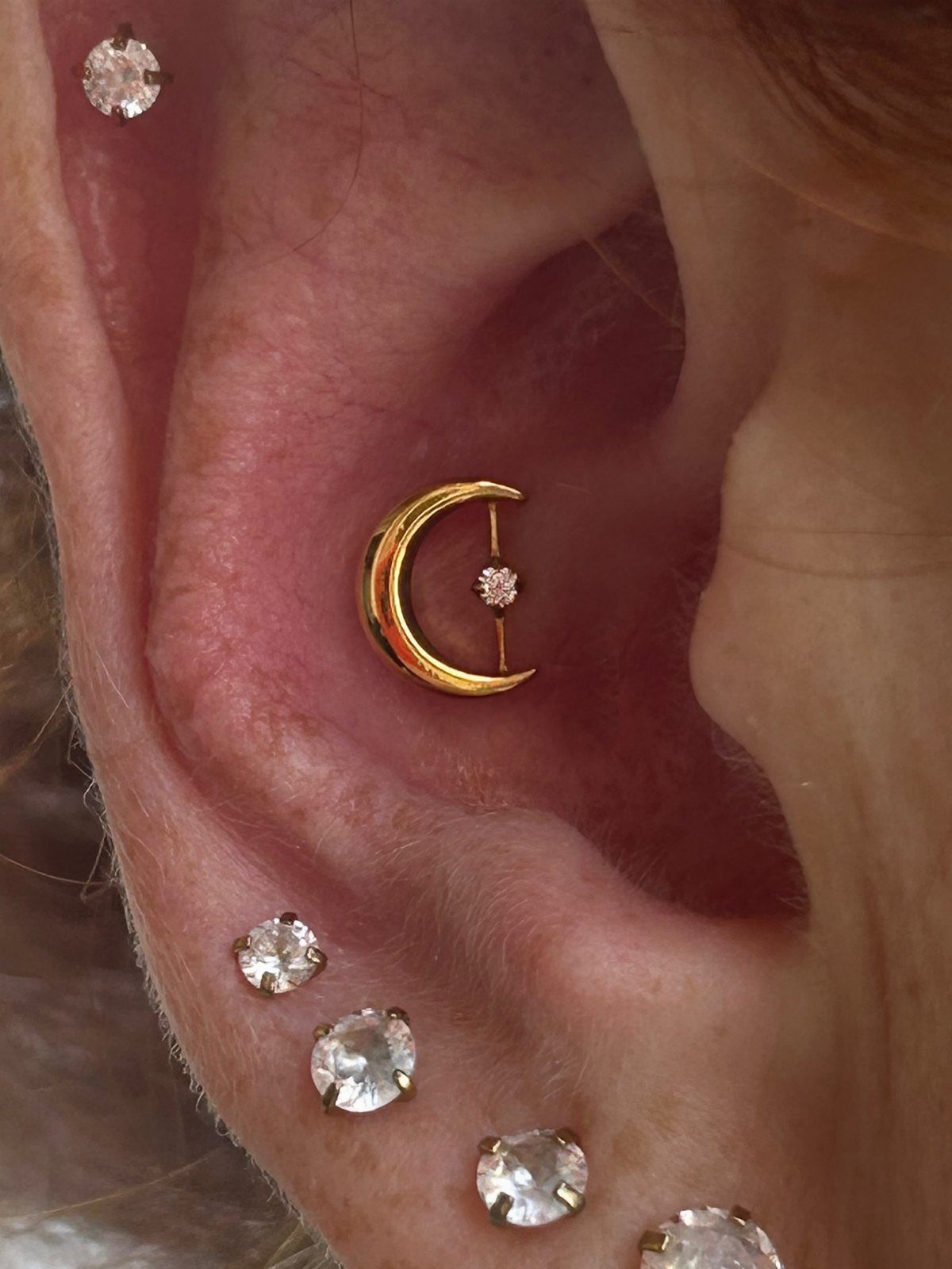 12 Ear Piercing Combo Ideas for Every Style 2 Ear with a gold crescent moon conch piercing and clear diamond lobe studs.