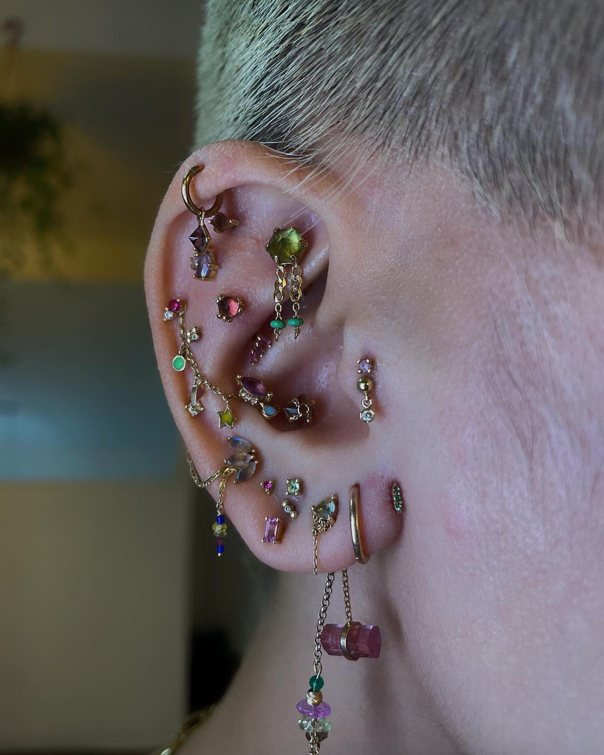 12 Ear Piercing Combo Ideas for Every Style 9 Ear with multiple gold and colorful gemstone piercings including a conch and constellation.