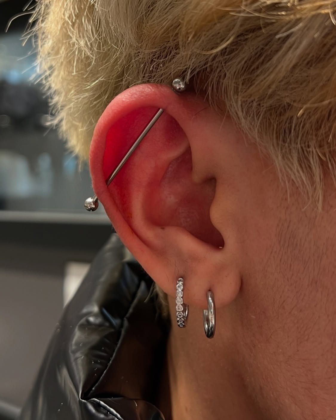12 Ear Piercing Combo Ideas for Every Style 5 Ear with a silver industrial barbell piercing and two small silver lobe hoops.
