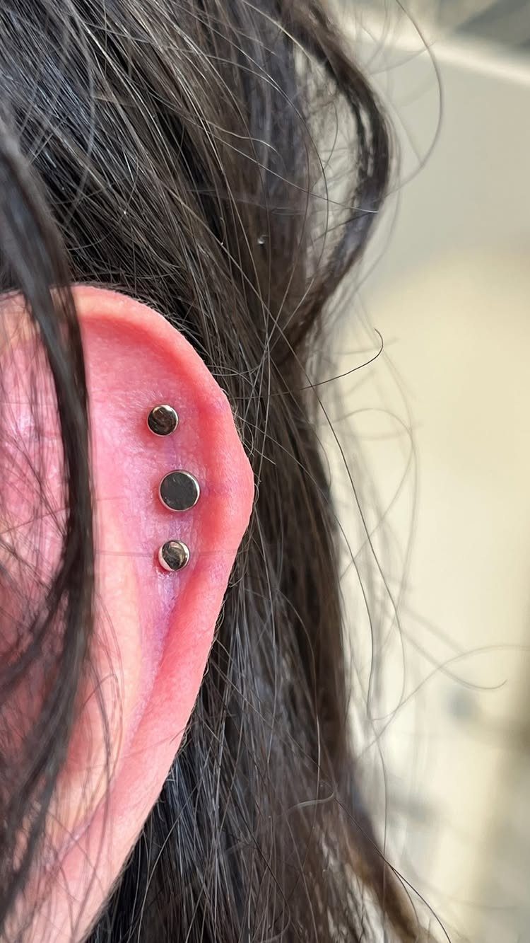 12 Ear Piercing Combo Ideas for Every Style 10 Ear with three silver stud piercings arranged vertically along the outer helix rim.