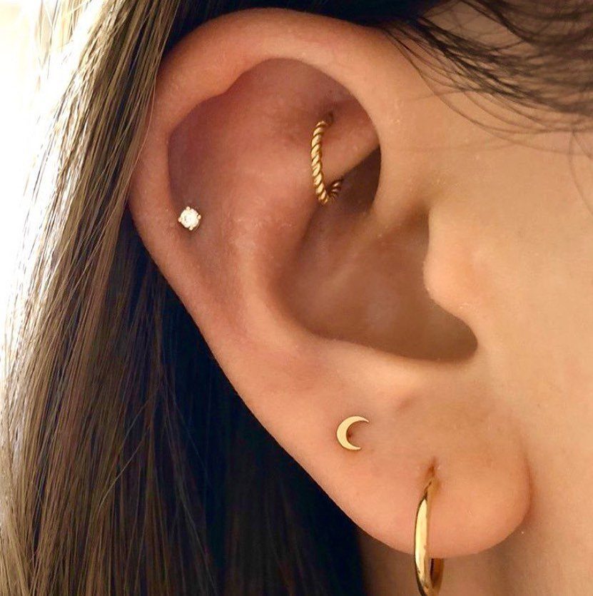 Ear with gold cartilage hoop, tragus stud, and lobe piercings including a moon stud.
