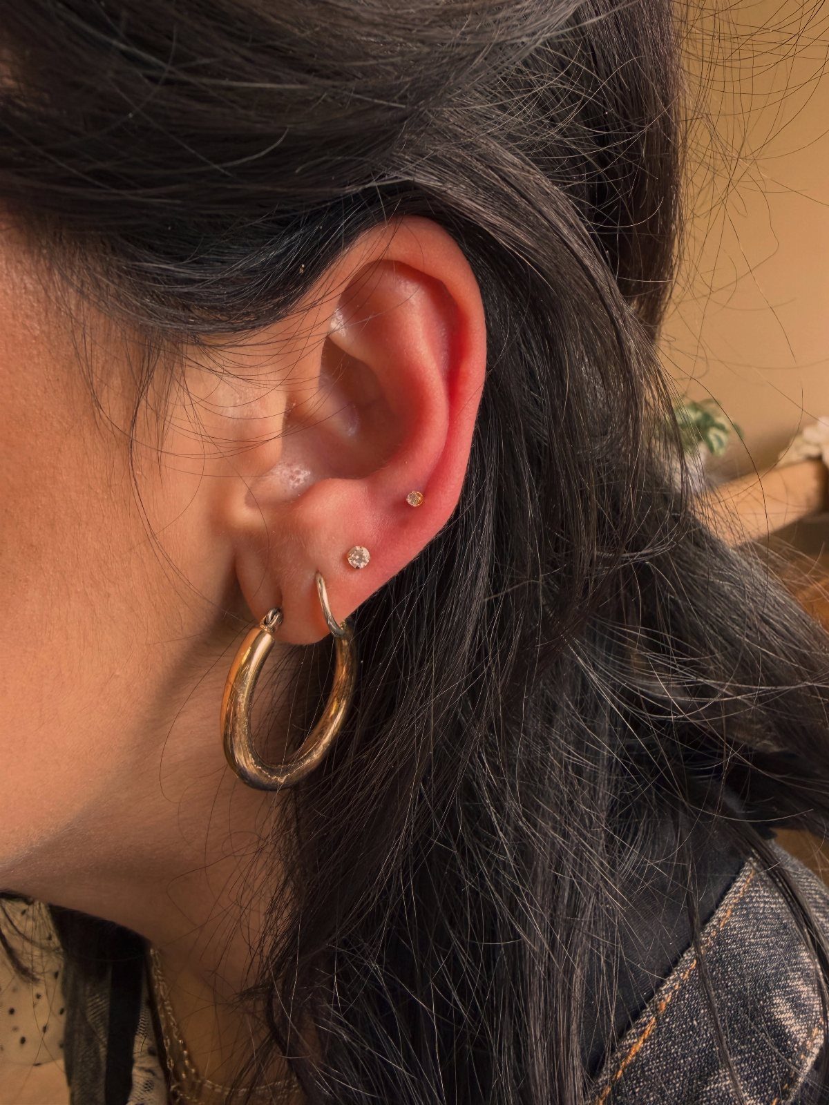 Gold hoop earring and small gold studs in a person's ear piercing.