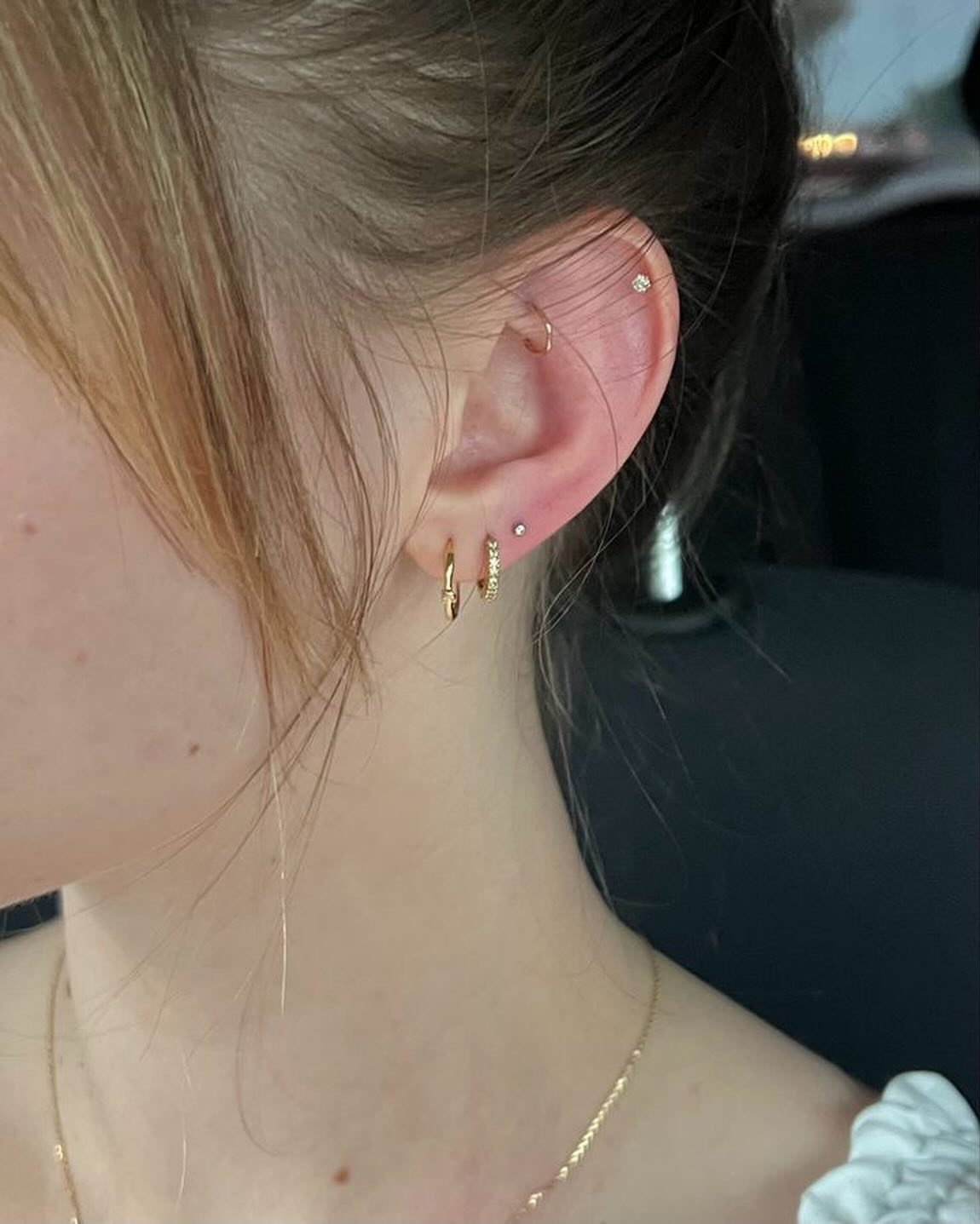 Ear with multiple gold hoop earrings and small studs in lobe and helix