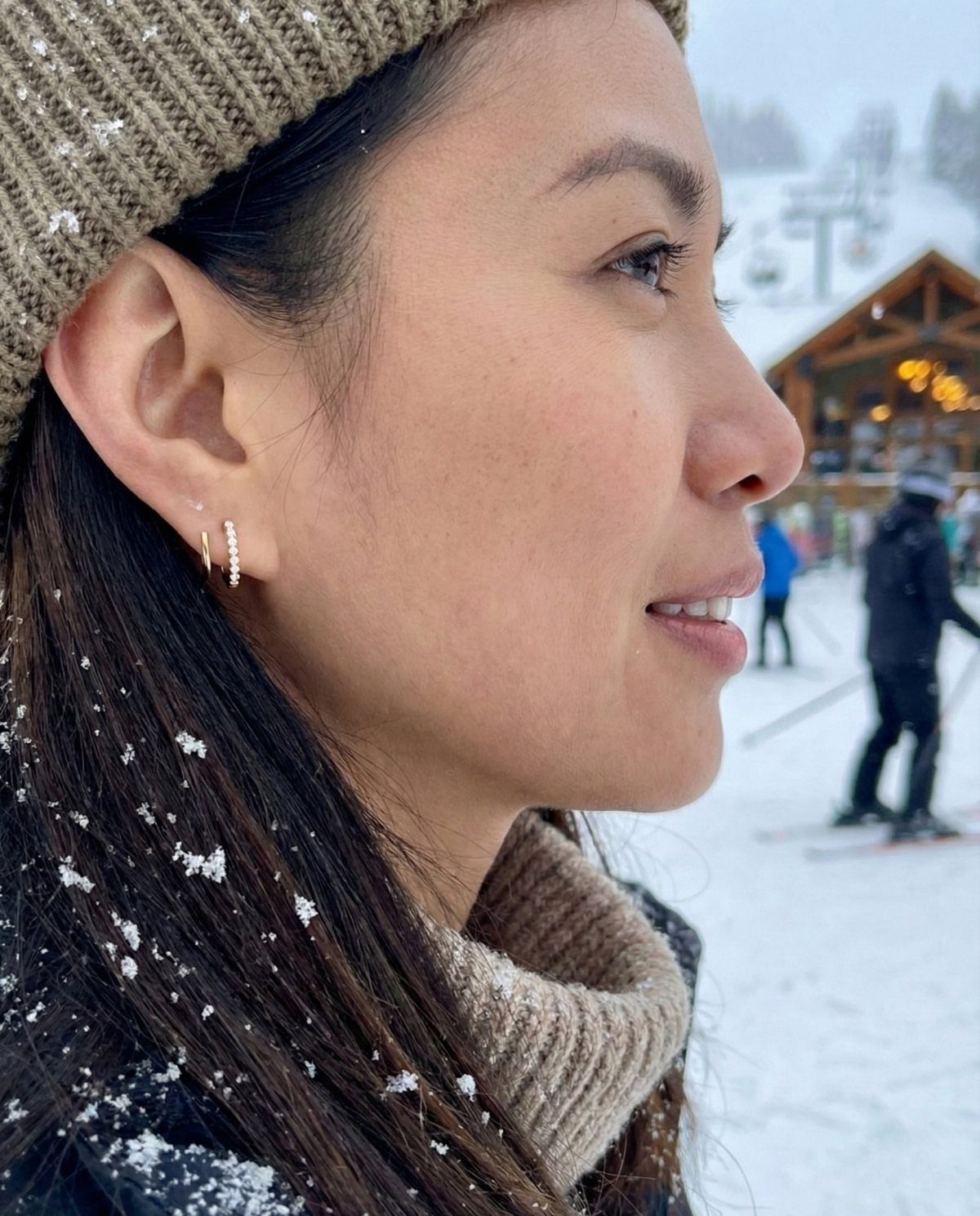 Woman in a beanie wearing small gold huggie hoop earrings in a snowy setting.