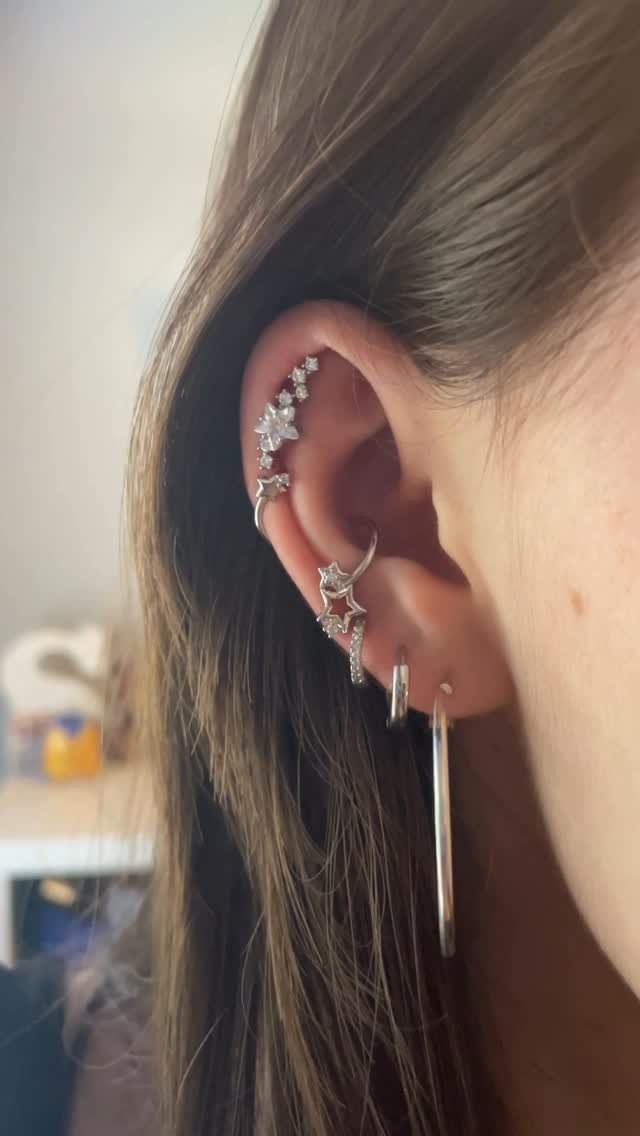 Ear with multiple silver hoop earrings and star-shaped cartilage jewelry piercings.
