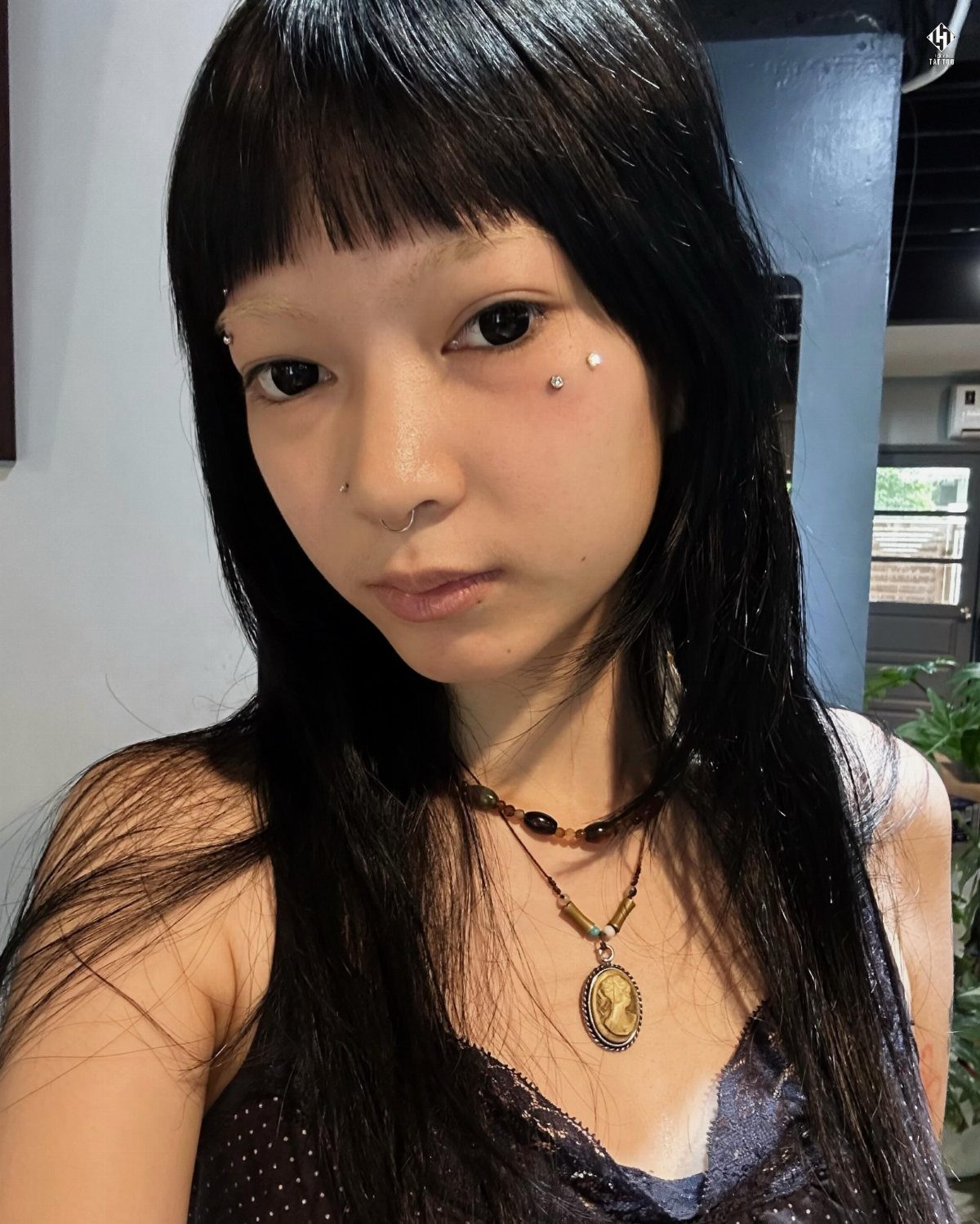 Woman with black hair featuring an anti-eyebrow piercing on her upper cheekbone.