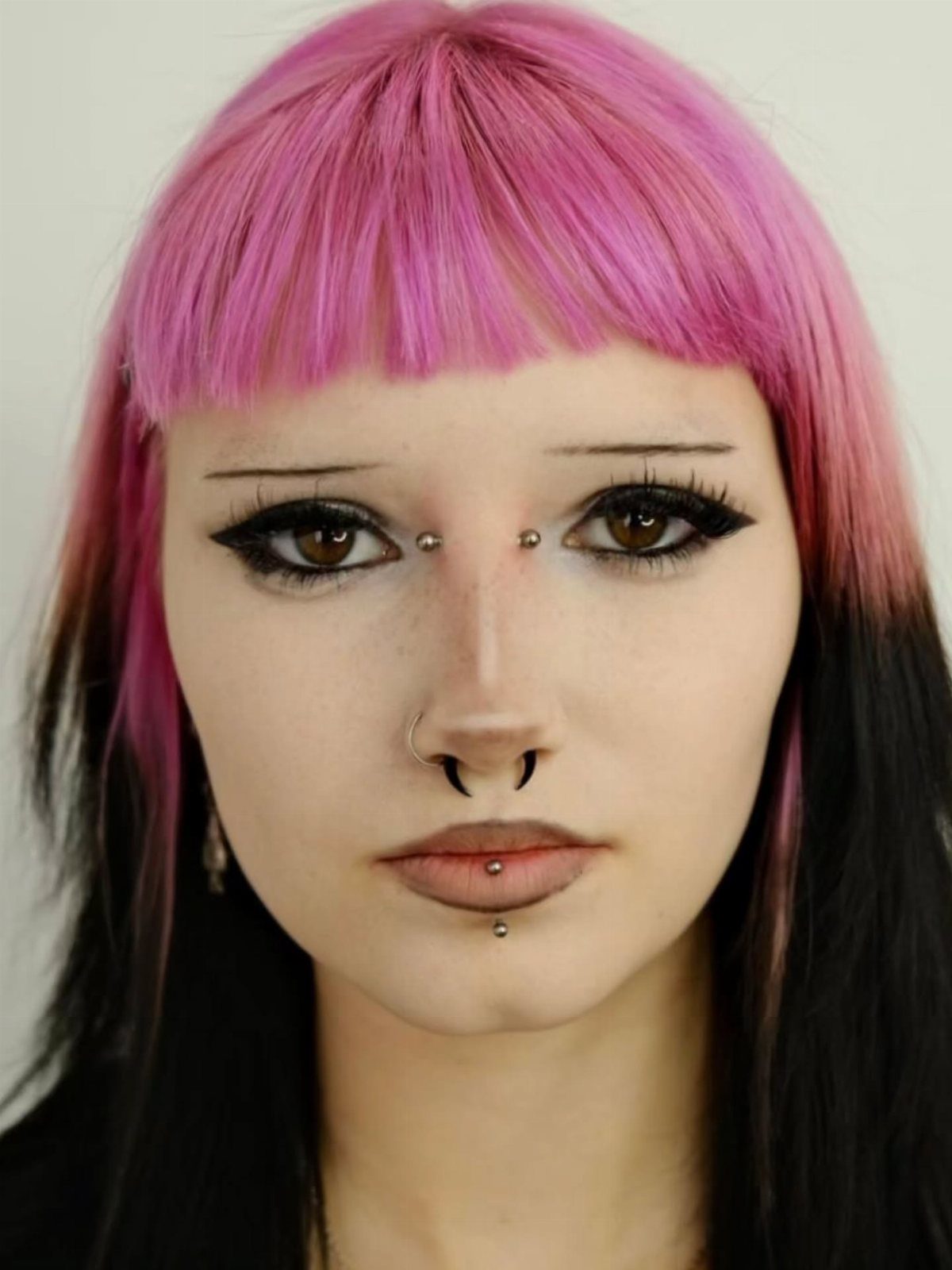 Person with pink hair and a bridge piercing, septum ring, and labret stud.