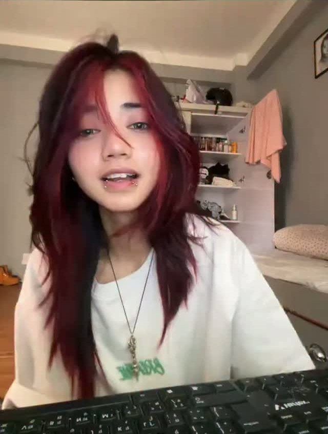 Young person with red hair and a labret lip piercing wearing a white shirt.