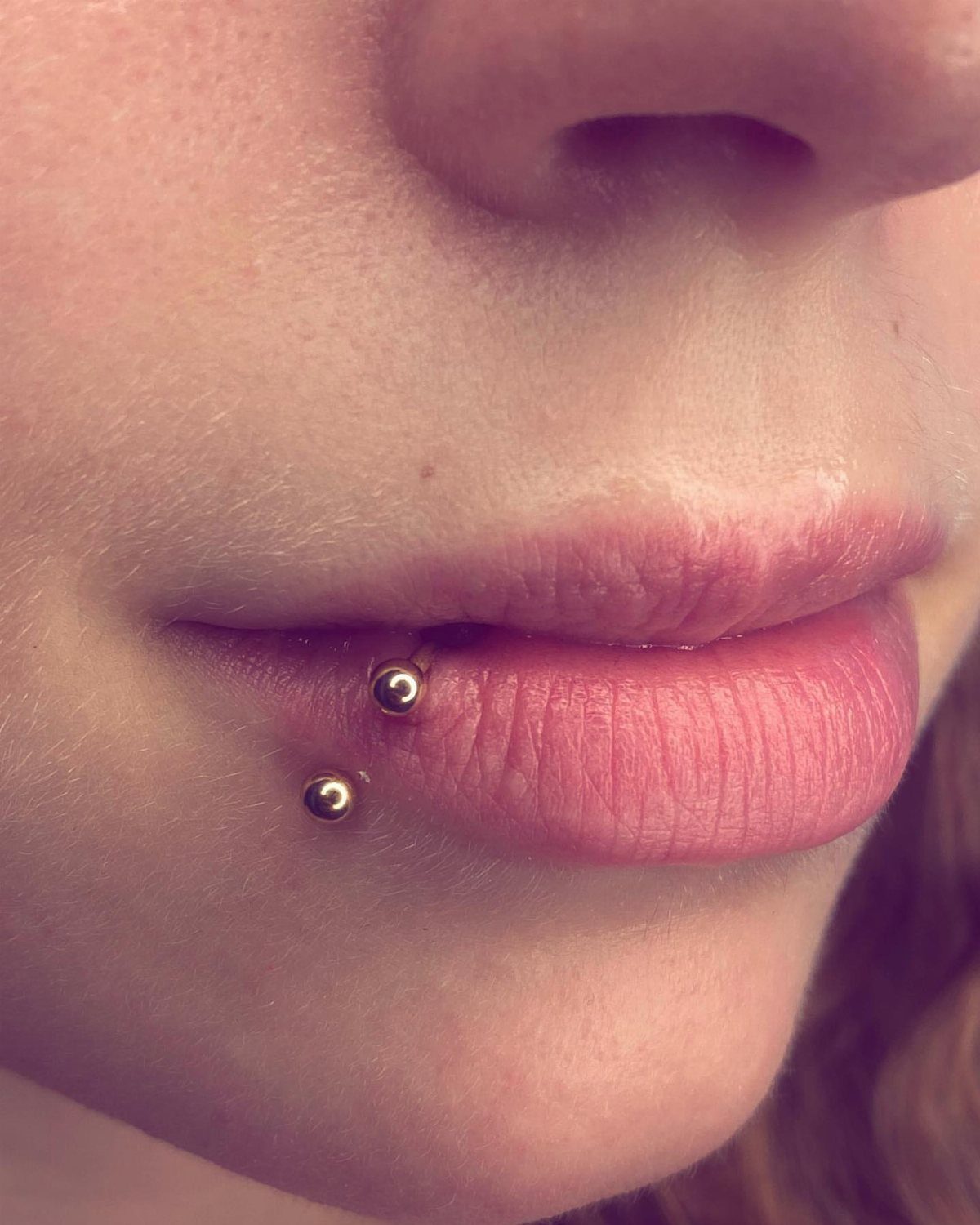 Lower lip with two gold ball stud piercings on the right side.