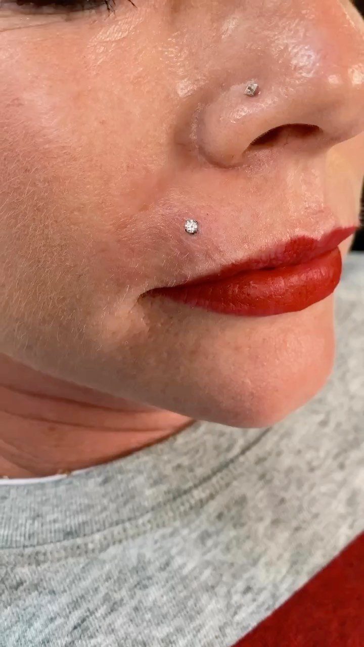 Person with red lipstick and a Monroe piercing and nostril piercing studs.