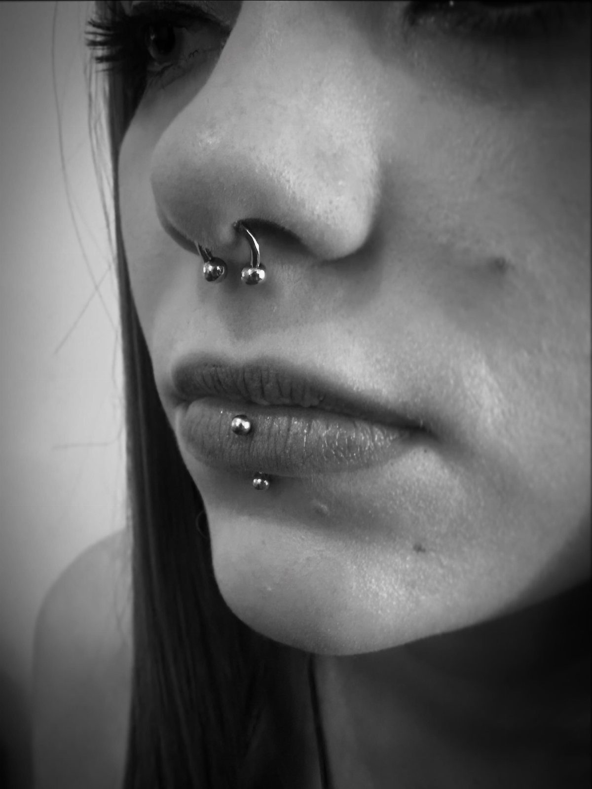 Person's face with a septum piercing and a vertical labret lip piercing.