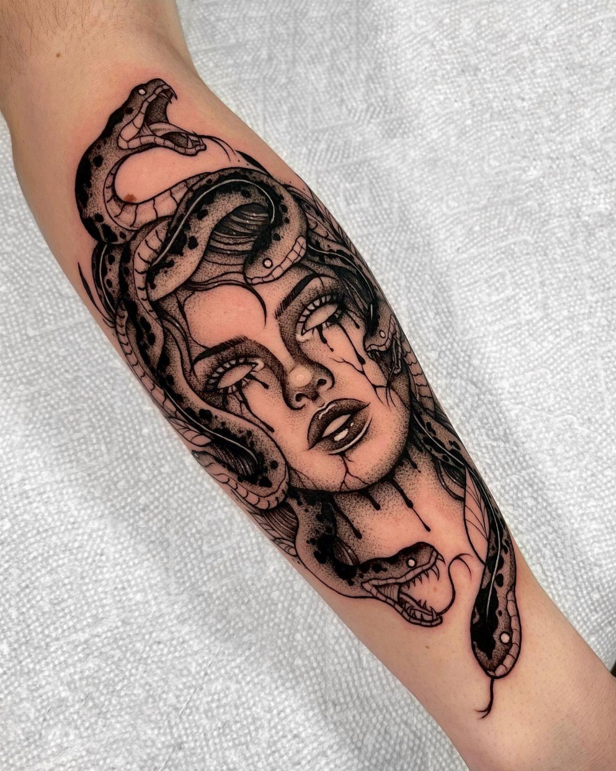 Feminine Medusa tattoo on a forearm with snakes for hair and crying eyes.