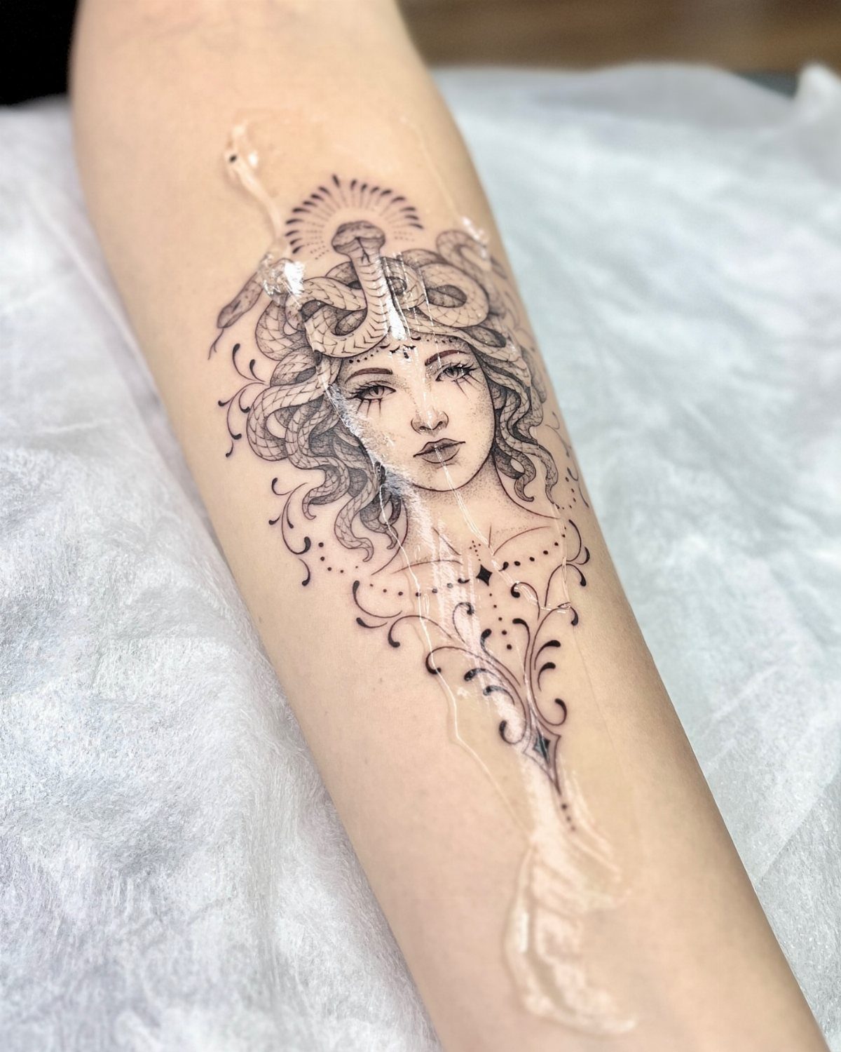 Feminine Medusa tattoo on a forearm with snakes and decorative ink patterns.