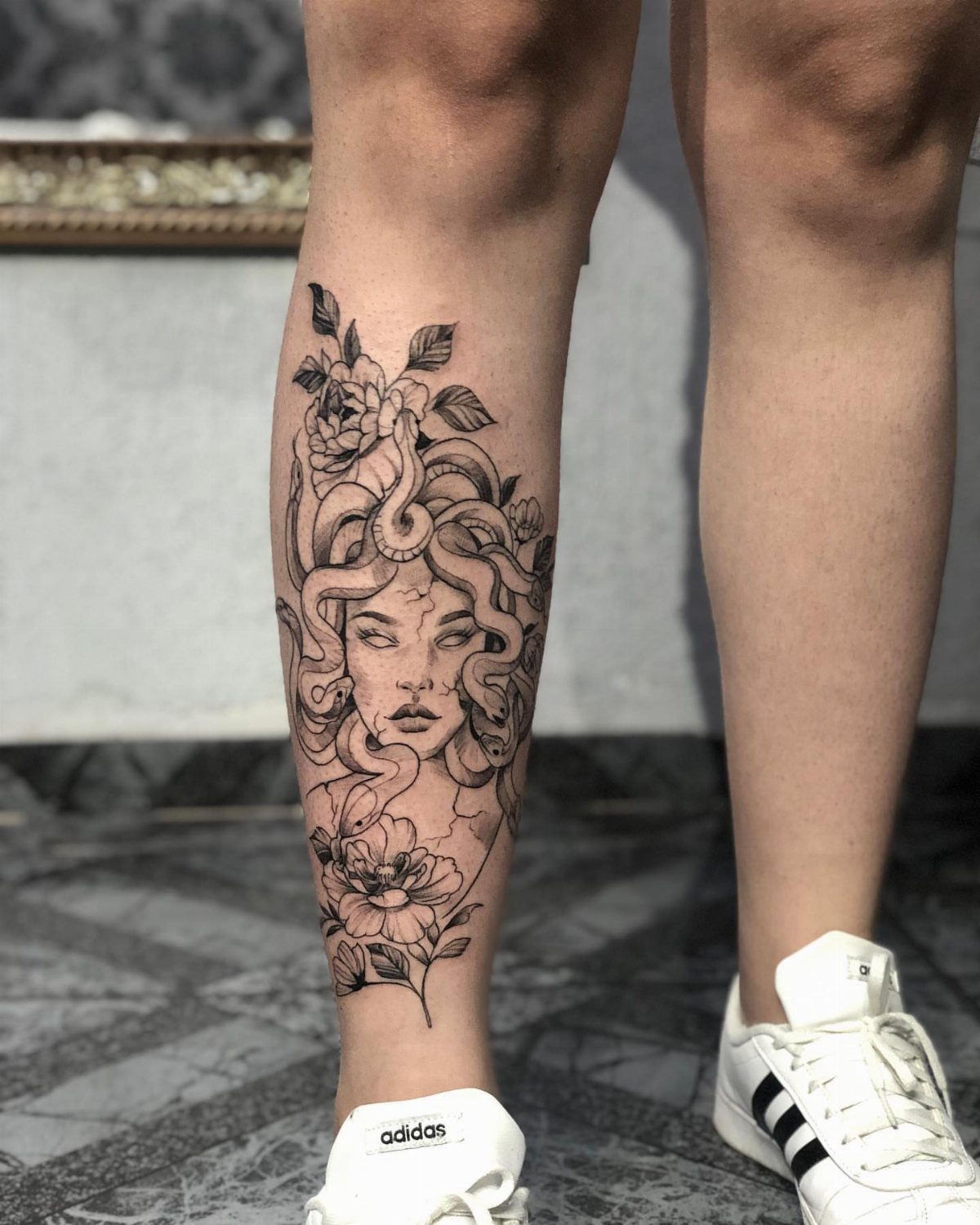 Feminine Medusa tattoo on a lower leg featuring snakes and floral elements.